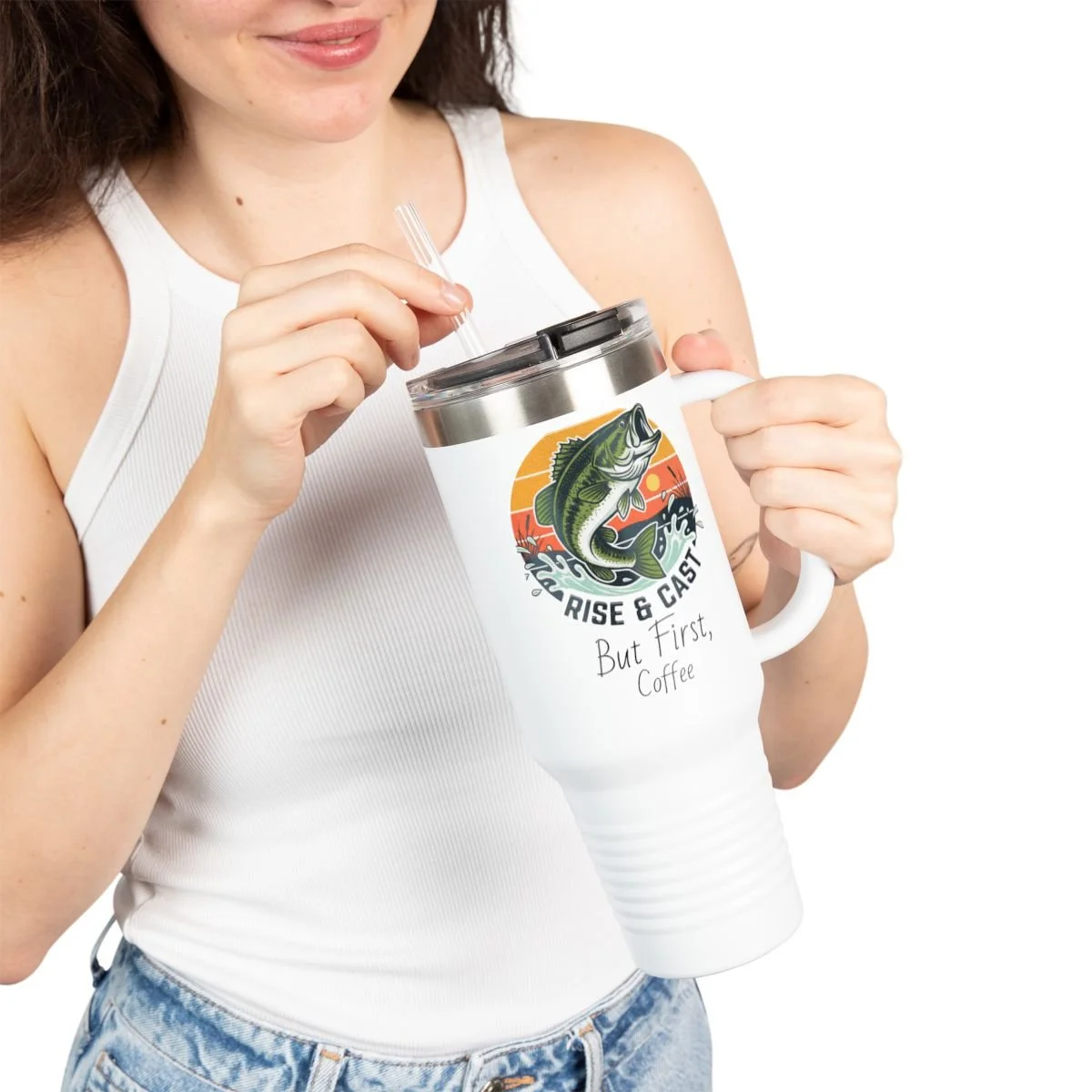 A woman in a white tank top holding a white travel mug with a fish illustration and the text 'Rise & Cast, But First, Coffee.' She is using a straw to drink from the mug.