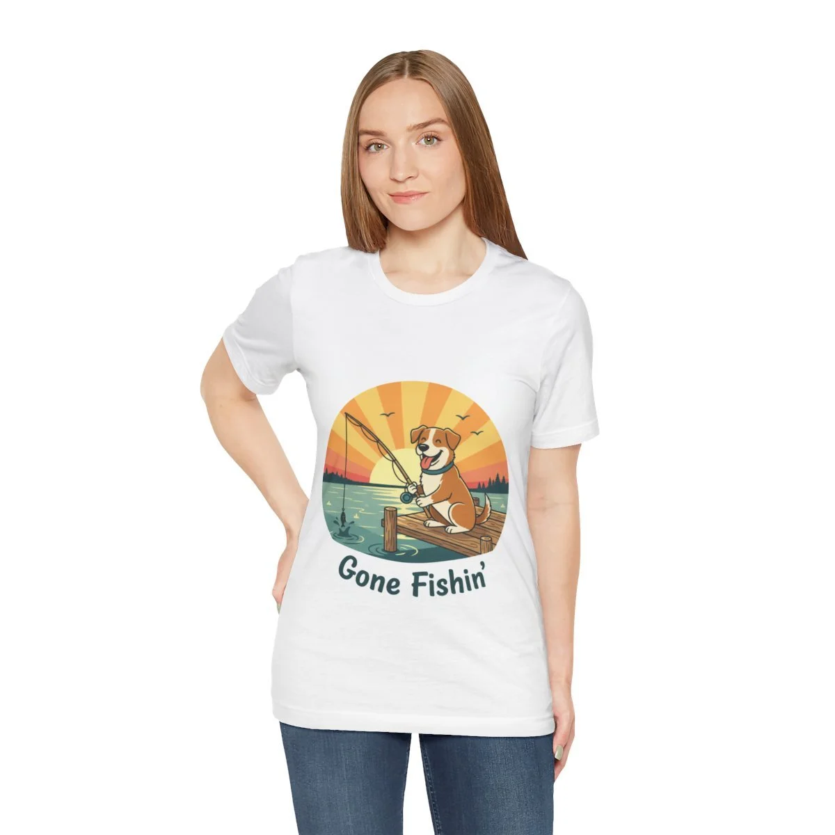 Young woman wearing a white T-shirt with a graphic of a dog fishing on a dock with a sunset, birds, and water, and the text 'Gone Fishin''.