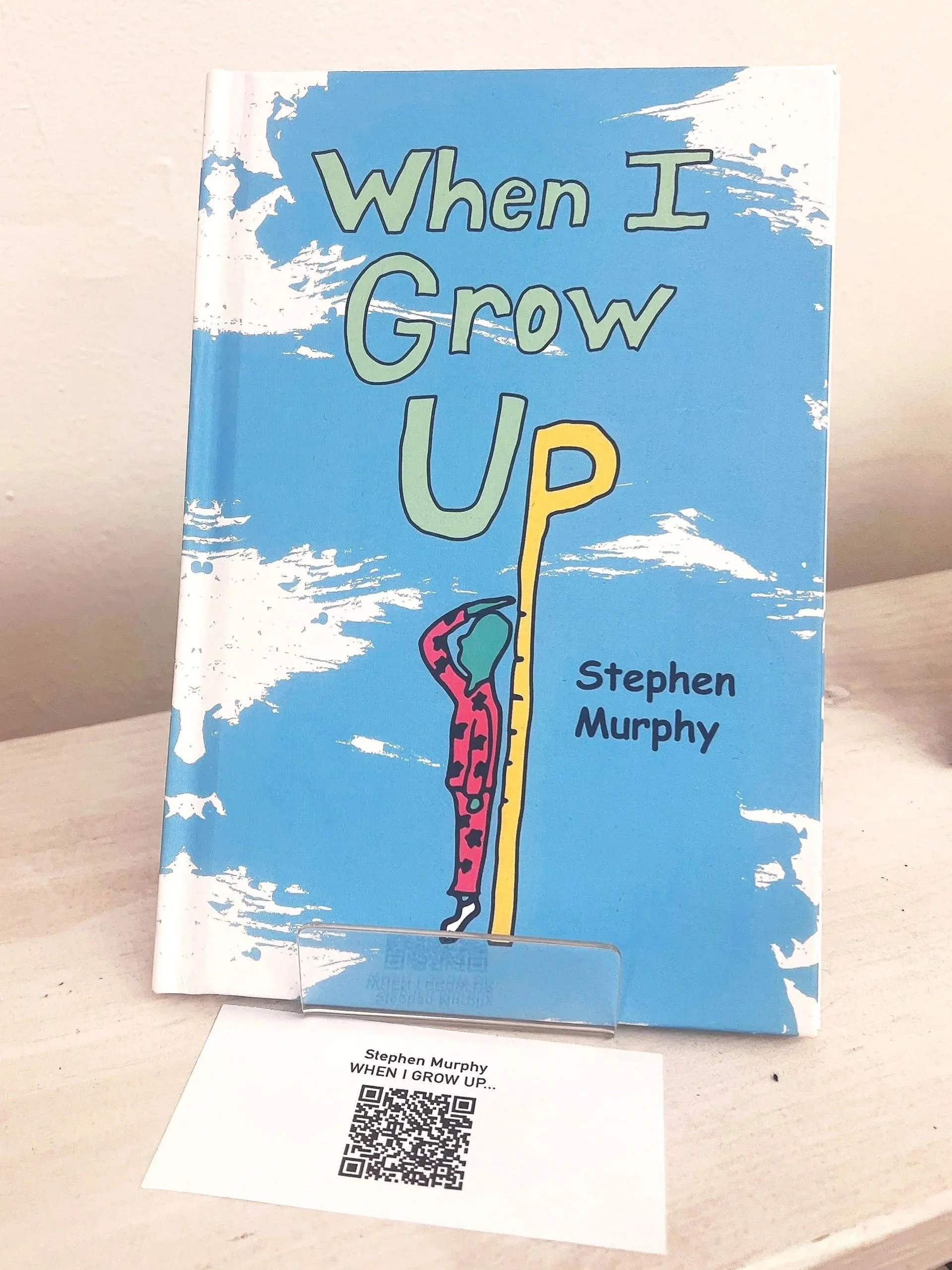 Book titled 'When I Grow Up' by Stephen Murphy standing upright on a desk with a QR code on a paper underneath it.