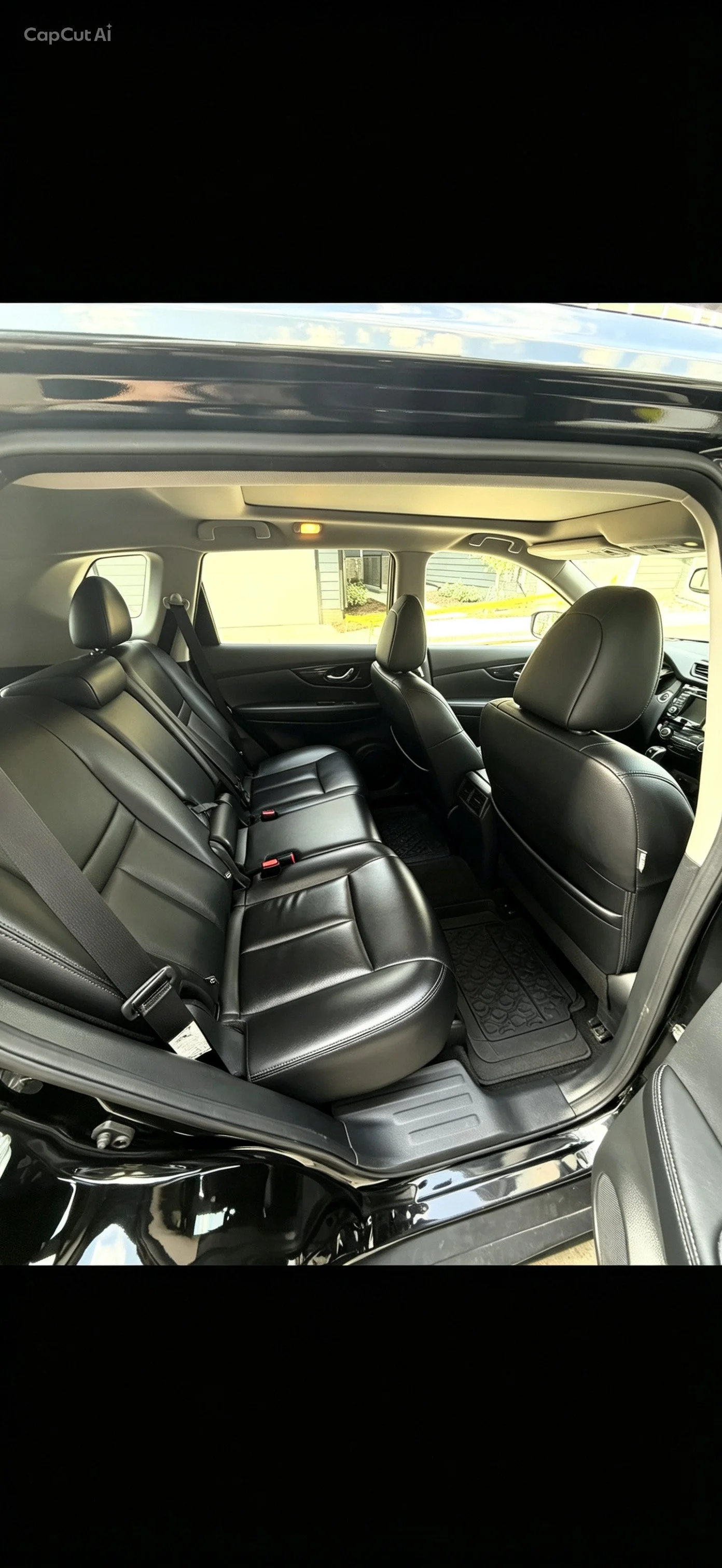 Interior view of a black SUV showing black leather seats, including rear and front passenger seats, with a view of the back window and a house outside.