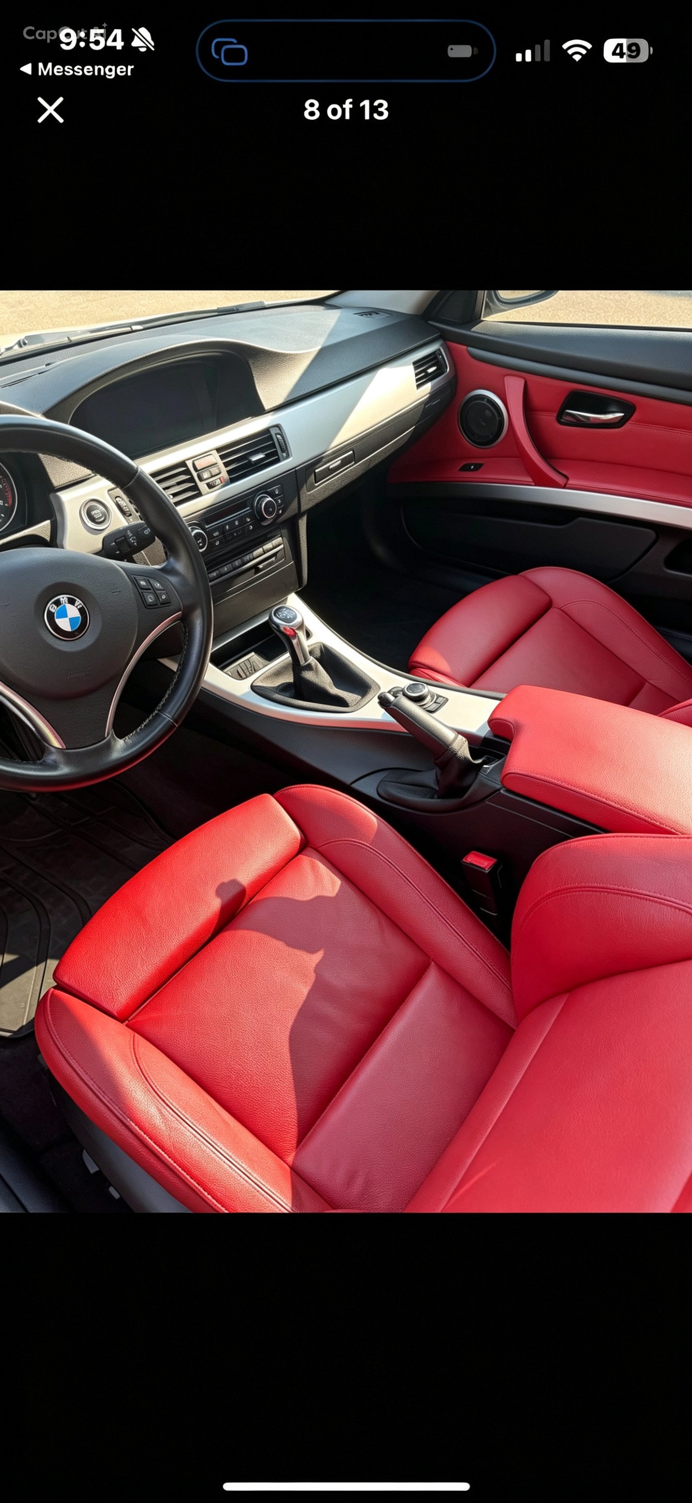 Interior of a BMW car with red leather seats, a black steering wheel with the BMW logo, and a dashboard with various controls and a gear shifter.