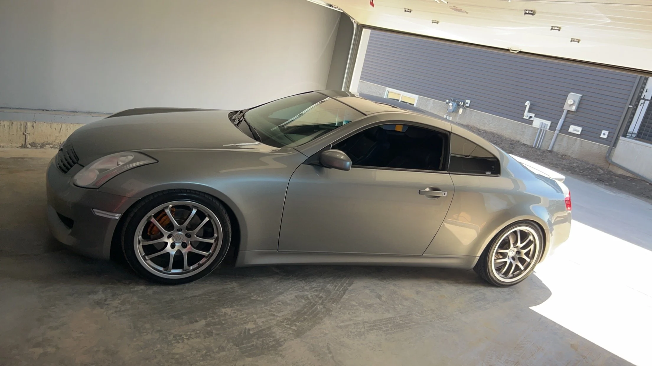 Silver sports car parked in an indoor garage with a partially open rolling door and gray walls