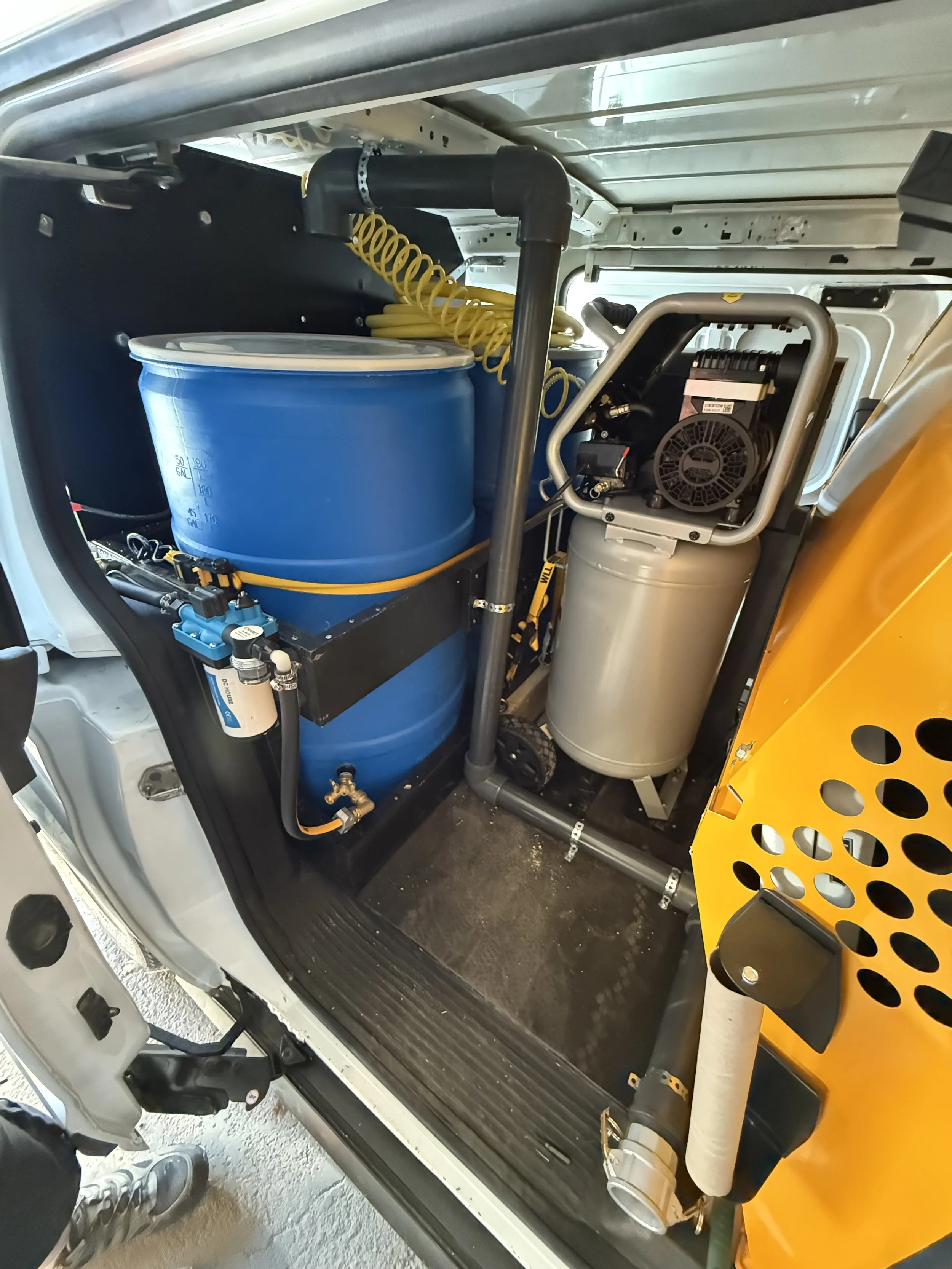 Inside an industrial vehicle, showing machinery, a blue container, a yellow hose, and mechanical components.