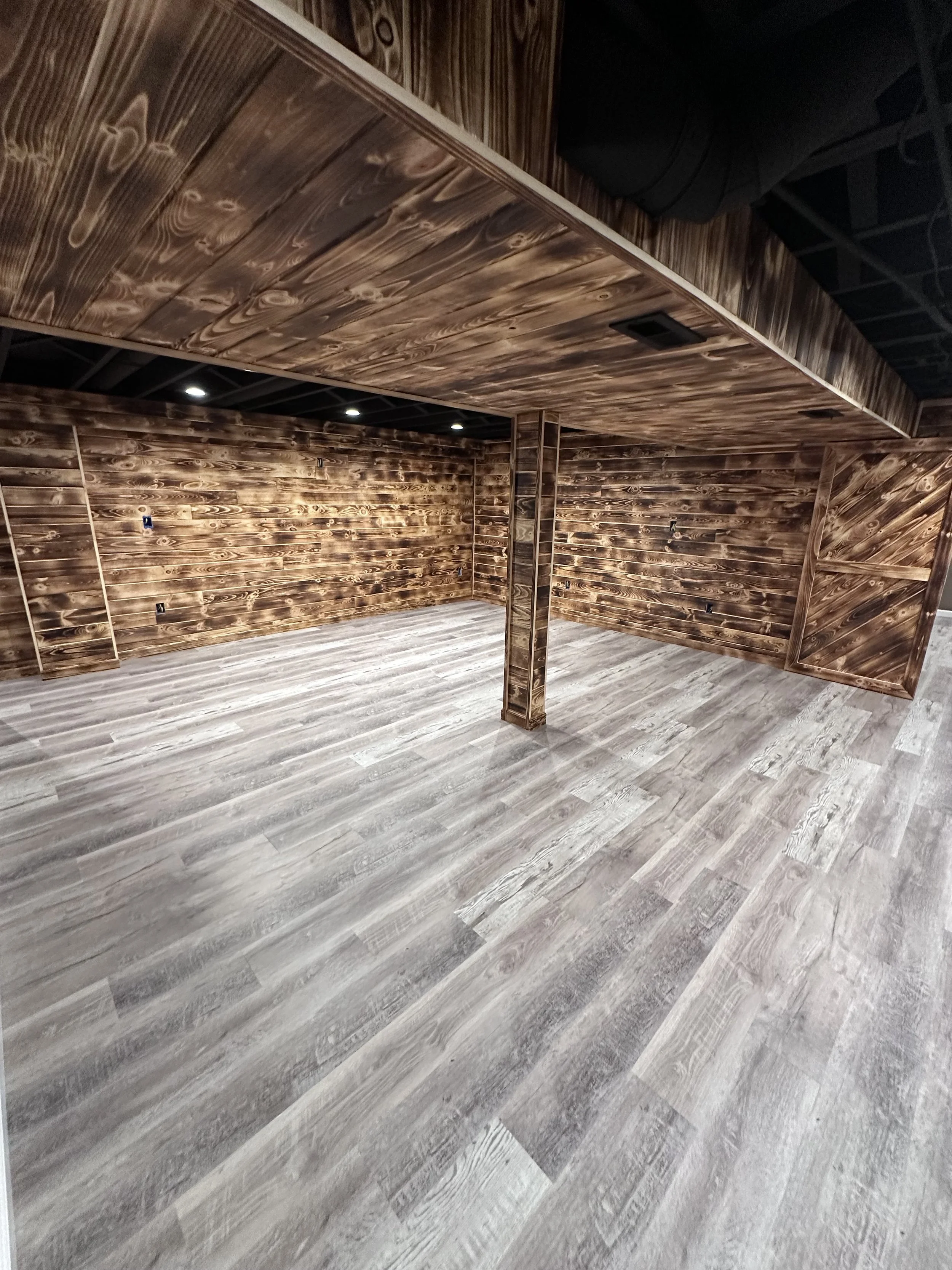 Basement room with white walls, partially finished ceiling with recessed lights, white cabinets, shelves, and wood-like flooring.