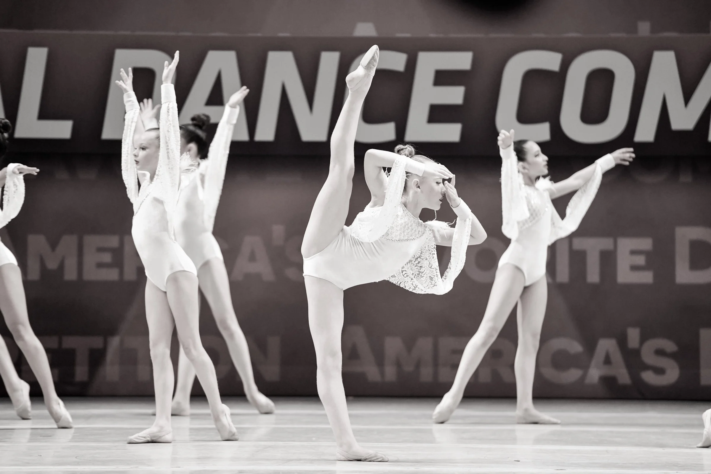 Young dancers in white costumes performing on stage with high leg extensions performing lyrical choreography at a dance conception-Studio-J-Dance-Collective-brea-fullerton-ballet-competition-team-dance-studio