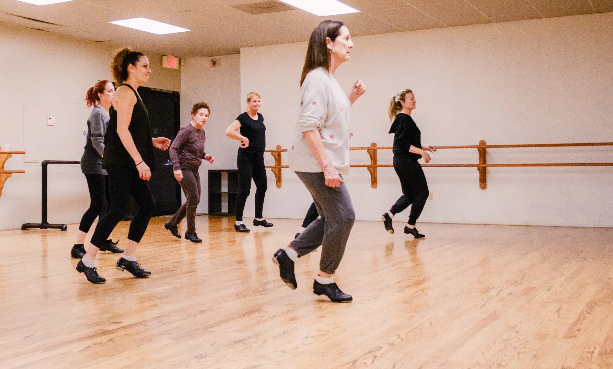 A group of women participating in an adult tap dance class, wearing tap shoes, at Studio J Dance- Tap technique class