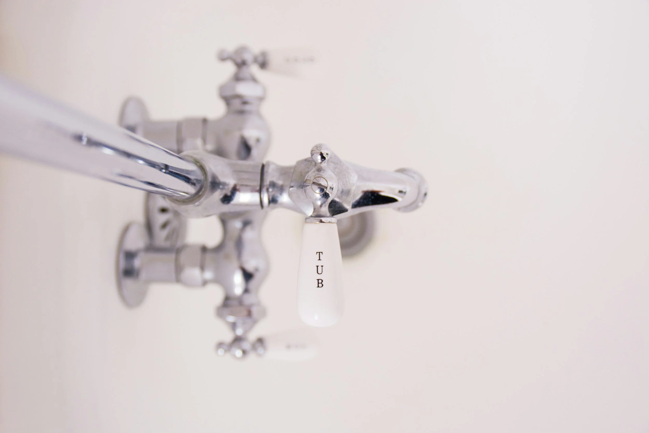 Close-up of a chrome water faucet with a white handle labeled 'TUB' against a plain white background.