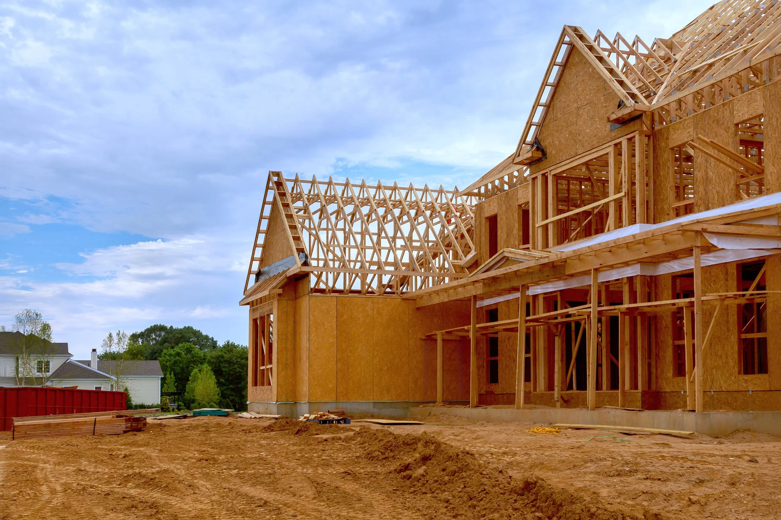 Wooden framing of a house under construction with blue sky and trees in the background.