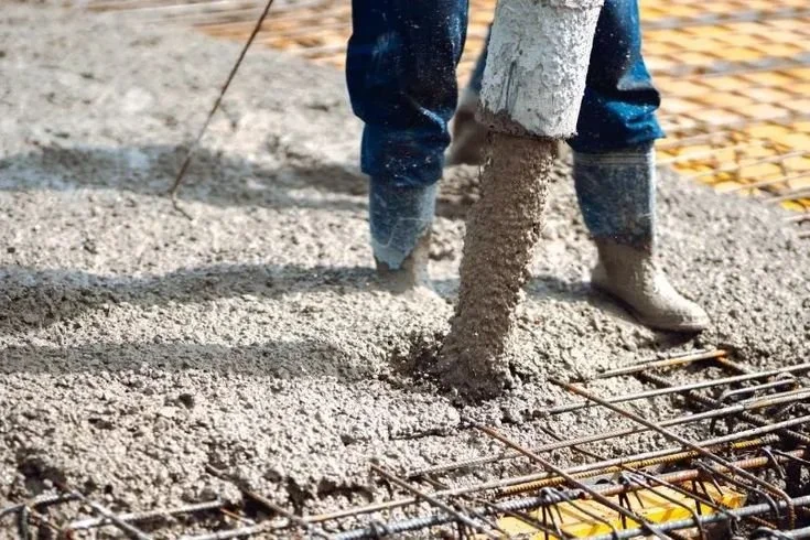 Person pouring concrete into a prepared area with rebar for a construction project.