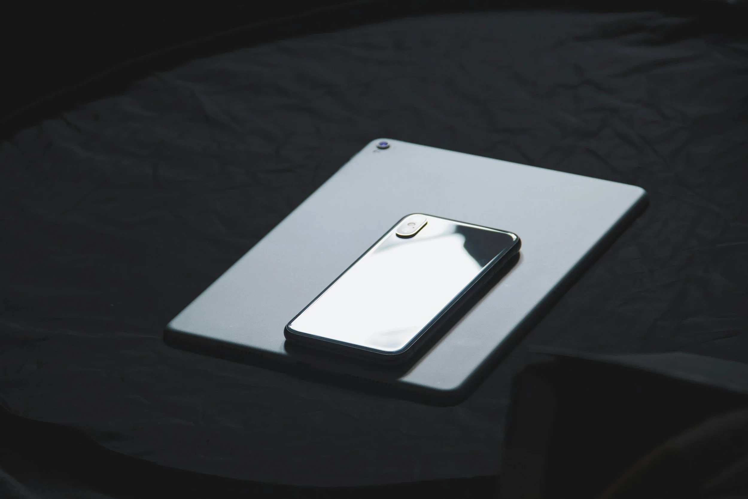 A modern smartphone with a reflective screen placed on top of a closed laptop, both on a dark textured surface.