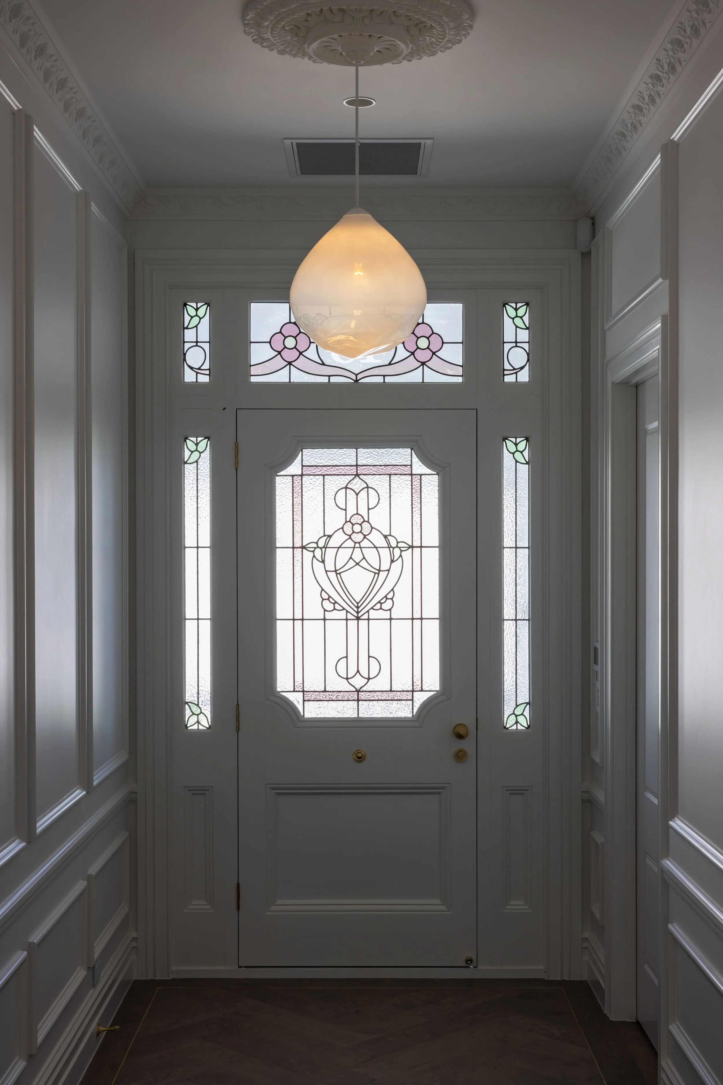 Front door with stained glass windows and a pendant light fixture in a white foyer.