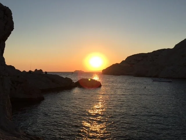 Sunset over a cove with rocky cliffs and a ship on the horizon.