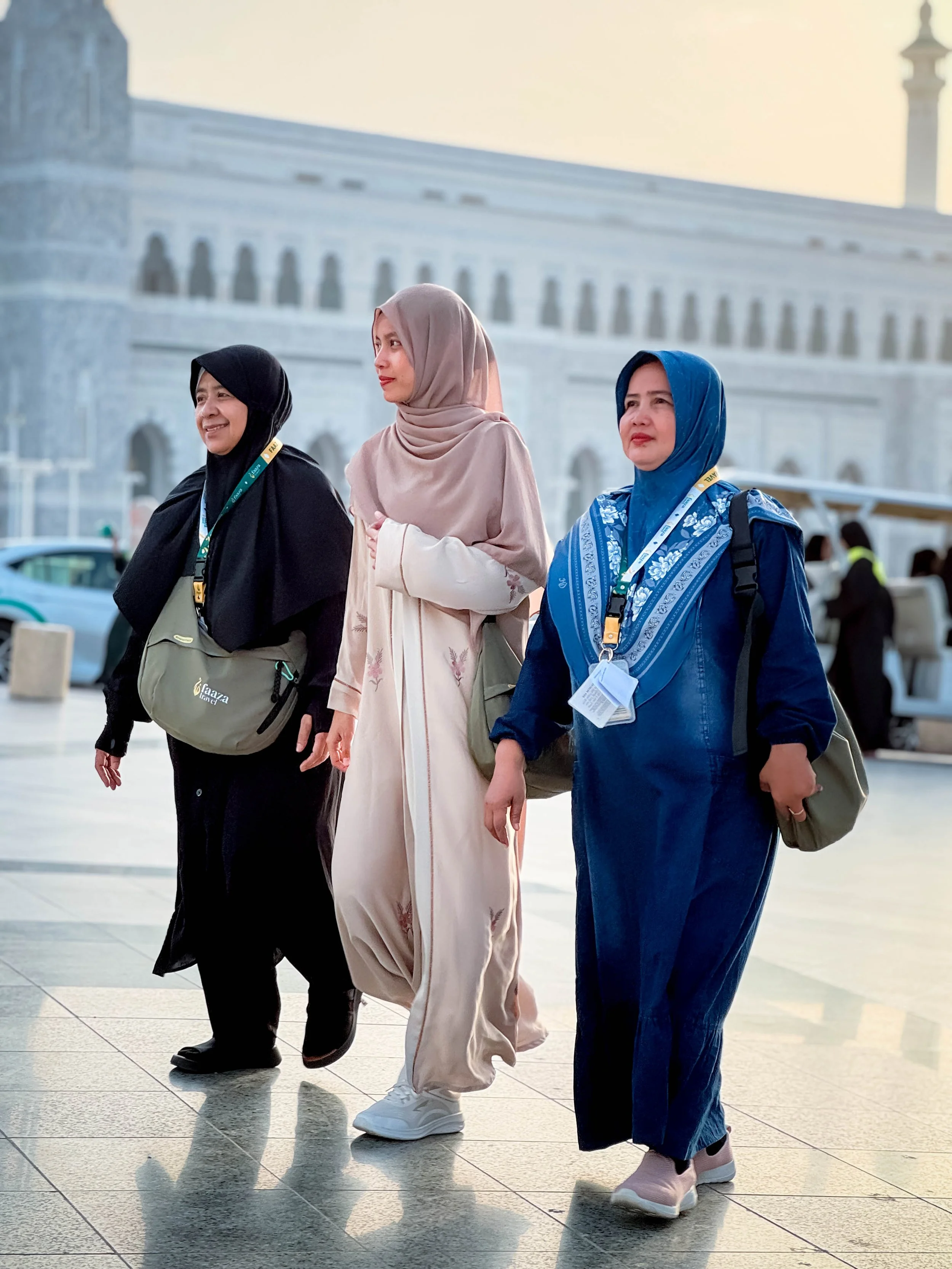 Three women walk together outside a government building, wearing casual clothes and face masks around their necks.