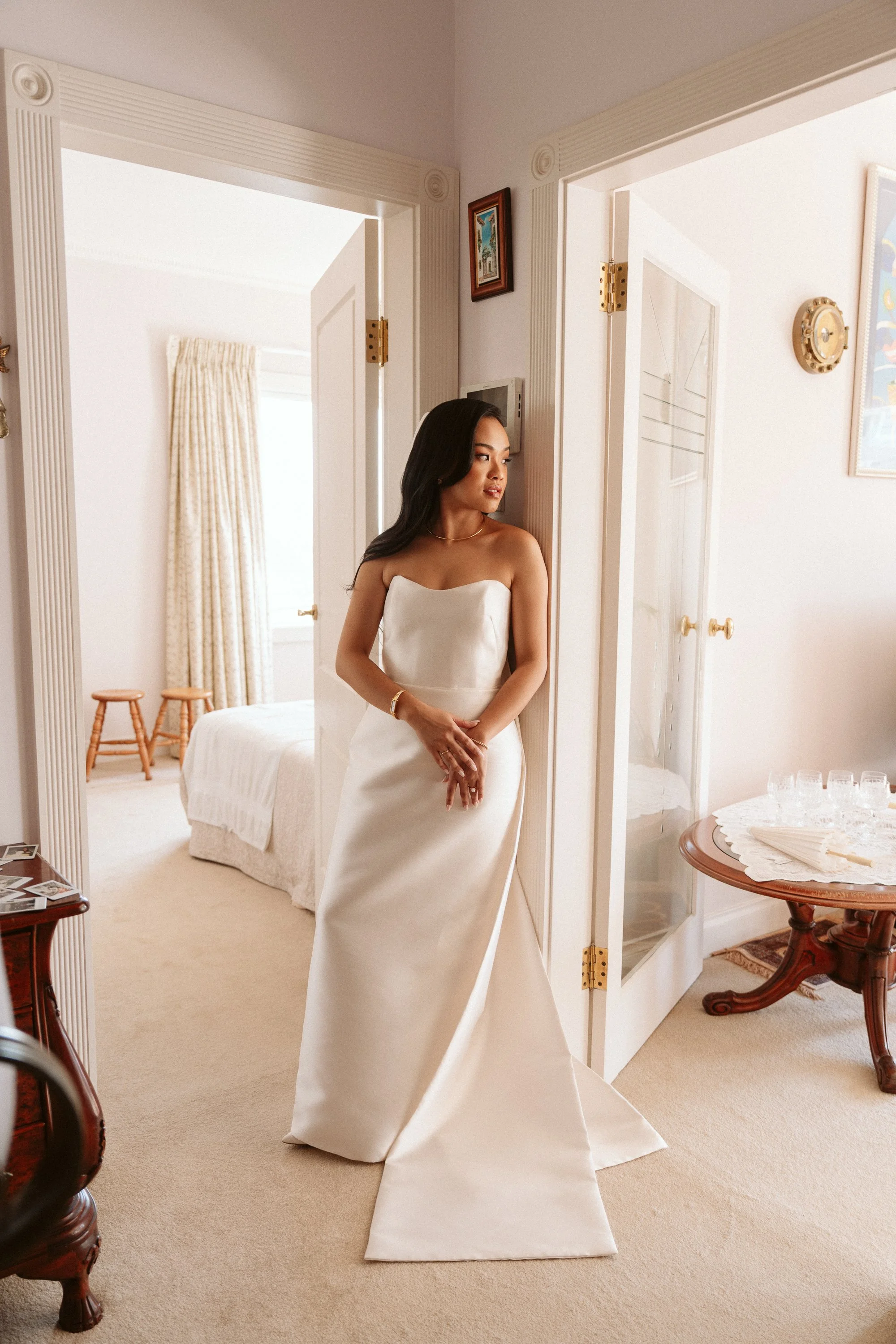 A woman in a strapless white wedding gown standing in a room, looking to her left.