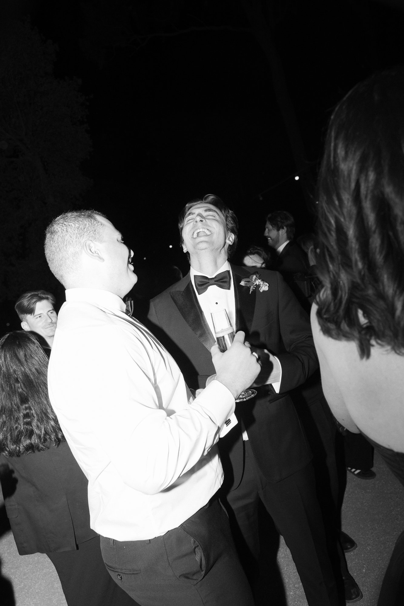 People at a formal event, with one man in a tuxedo holding a glass of drink, laughing and enjoying the moment.