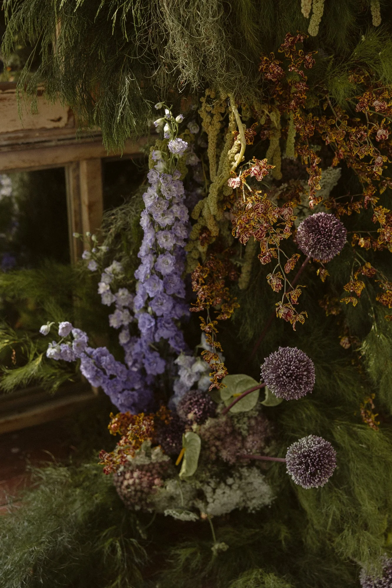 Close-up of a decorative floral arrangement with purple, white and dark round flowers, and various greenery.