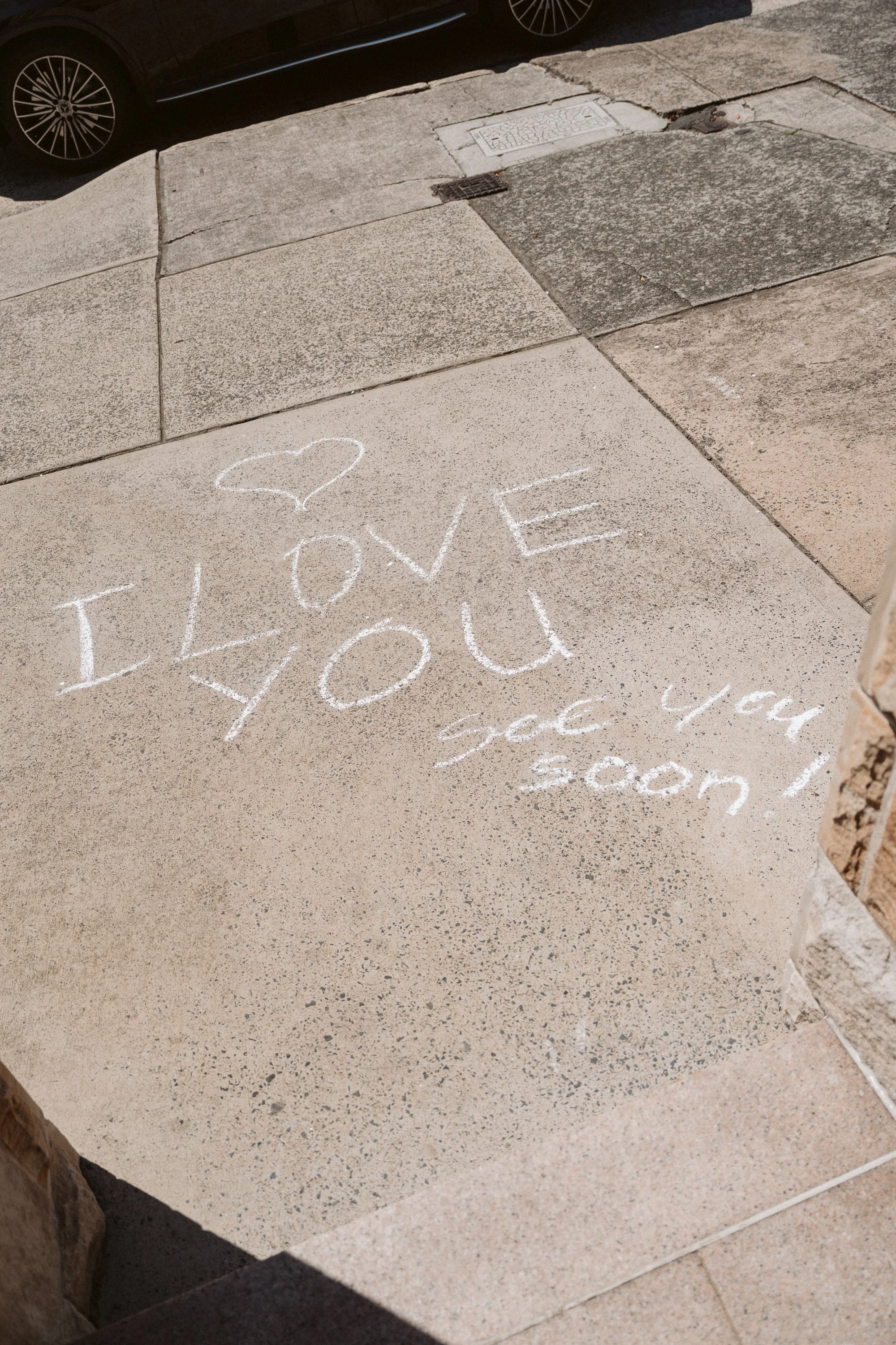 Chalk writing on concrete sidewalk that says "I love you" with a heart above it, and some partially visible text below.