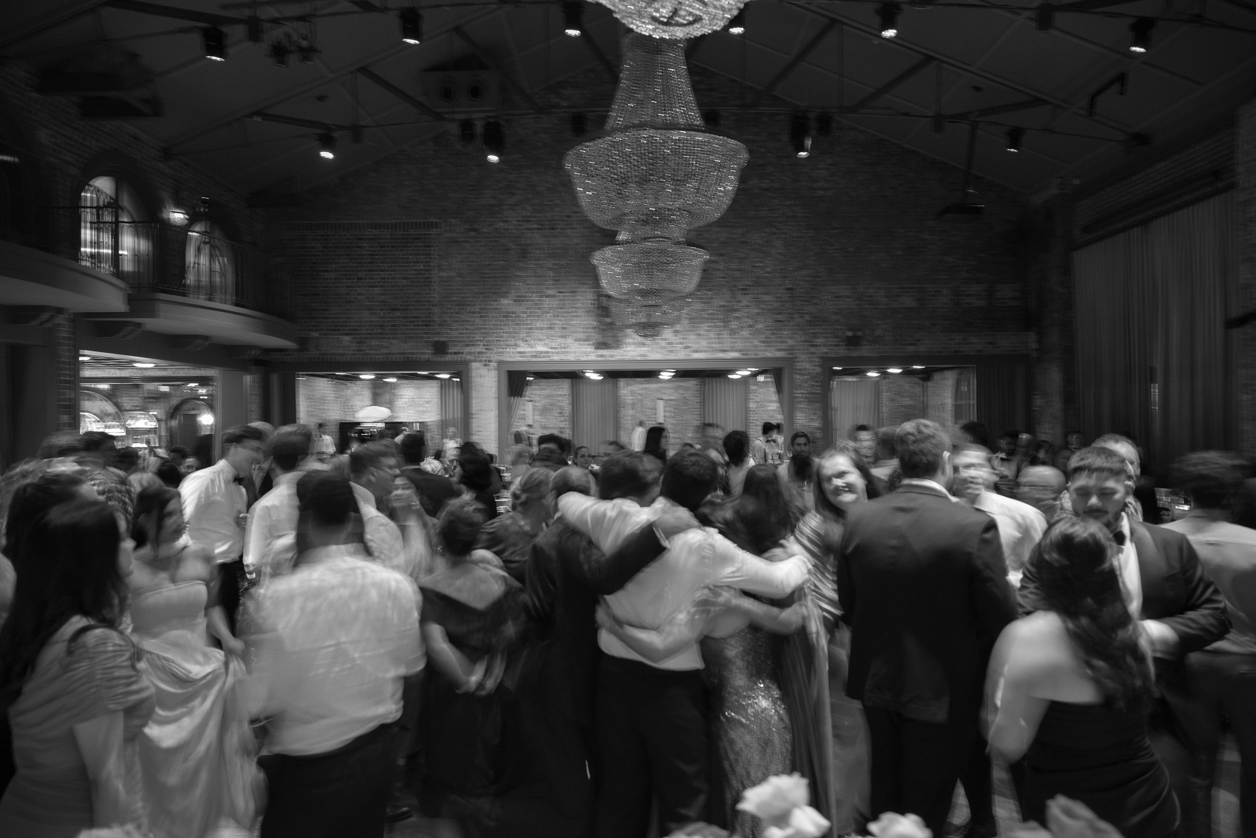 A black-and-white photo of a crowded indoor party with people dancing and socializing under a chandelier.