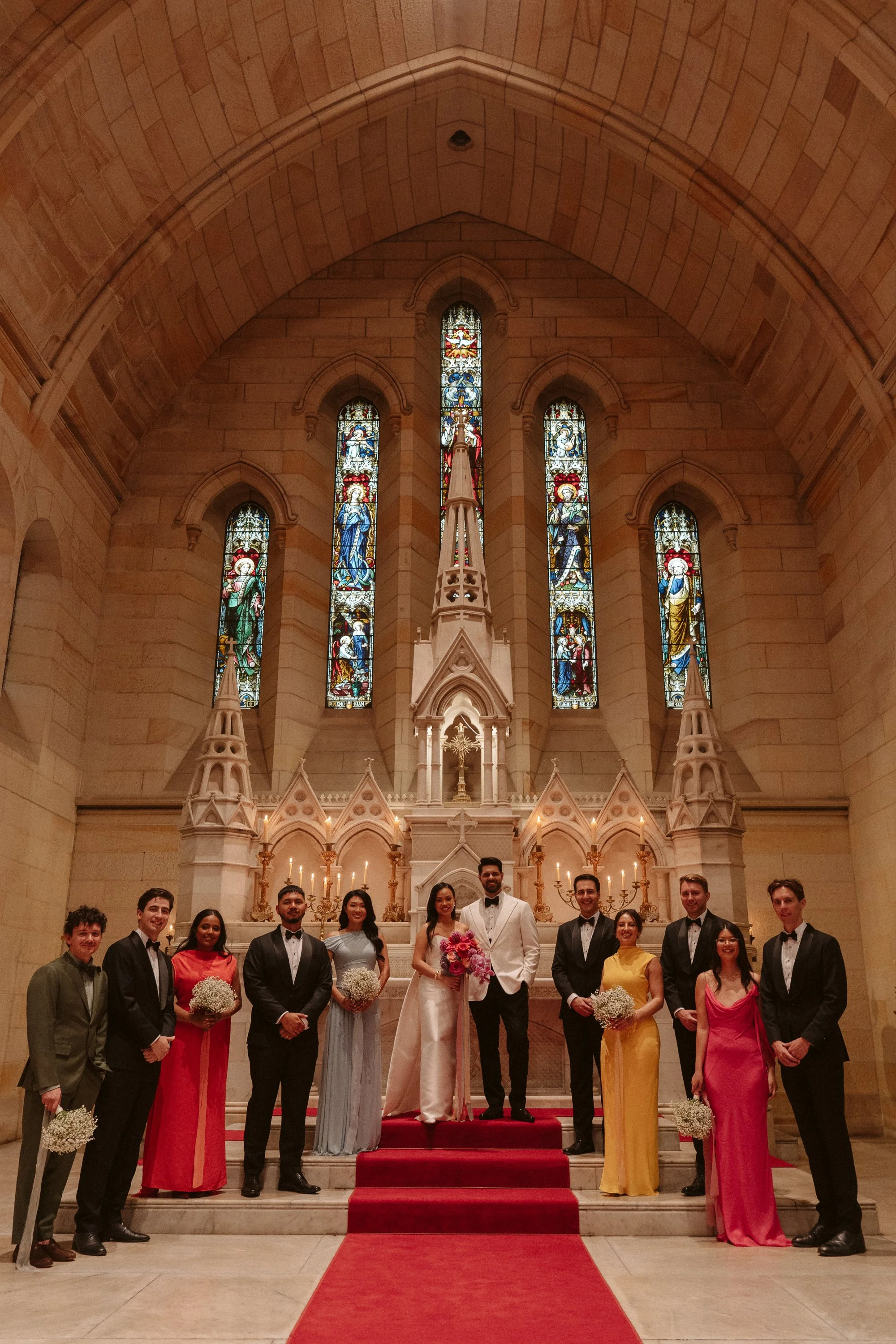 A wedding party standing inside a church, with stained glass windows and an altar in the background.