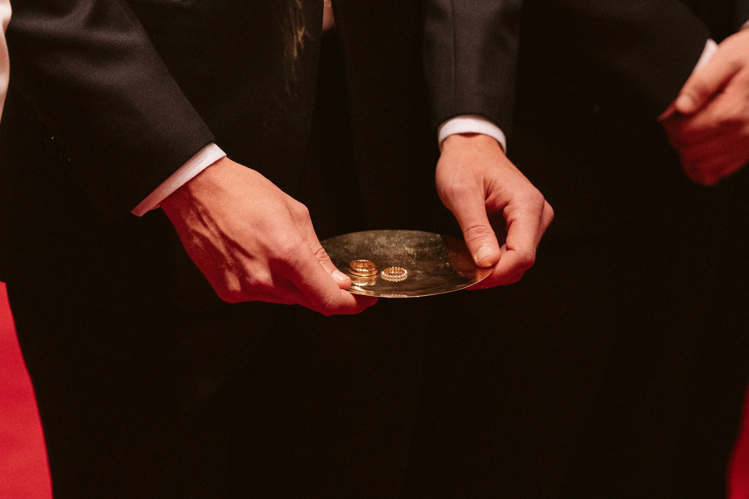 Hands of a person in formal attire holding a tray with wedding rings.