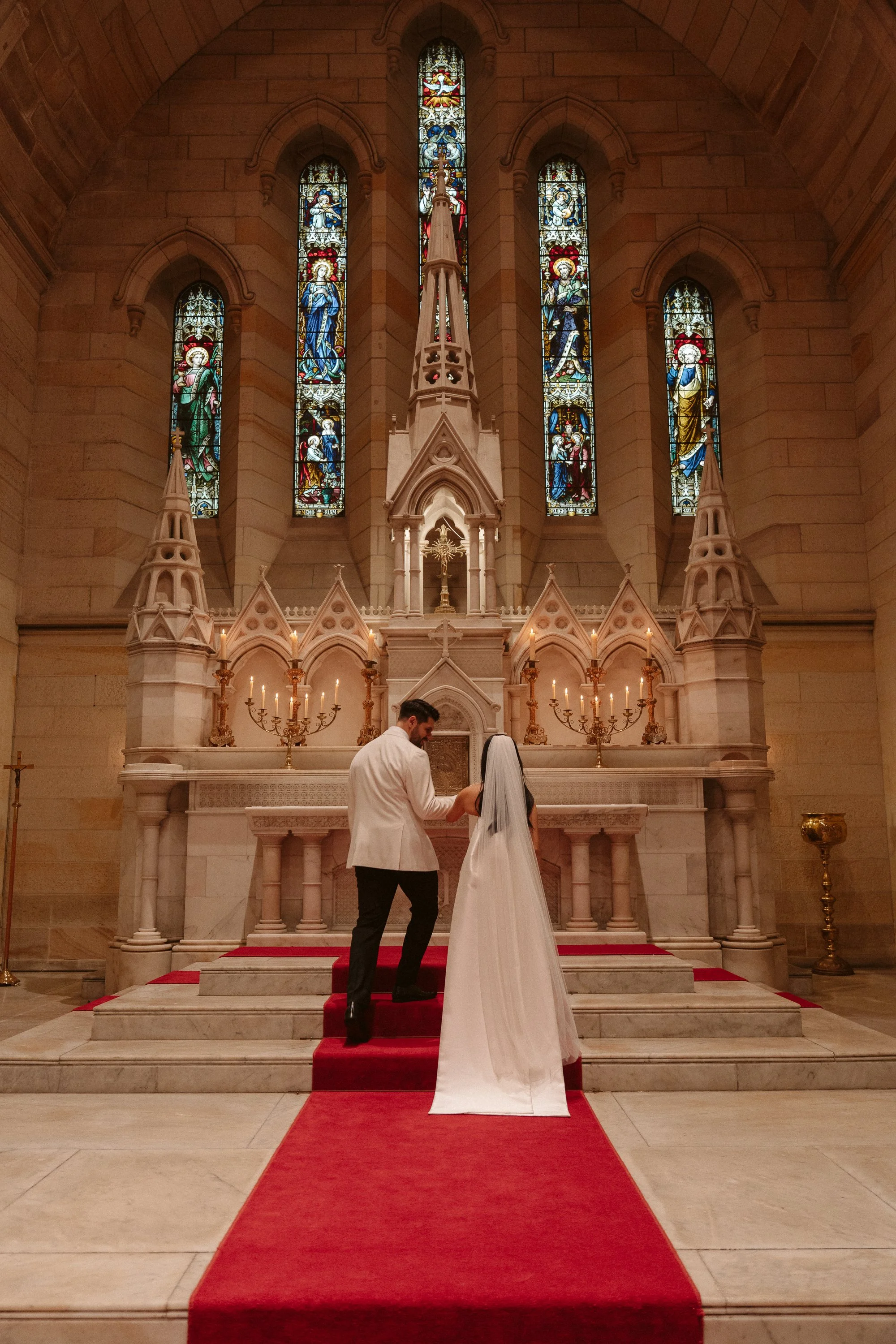 A bride and groom exchanging rings at the altar of a church during a wedding ceremony, with stained glass windows in the background.
