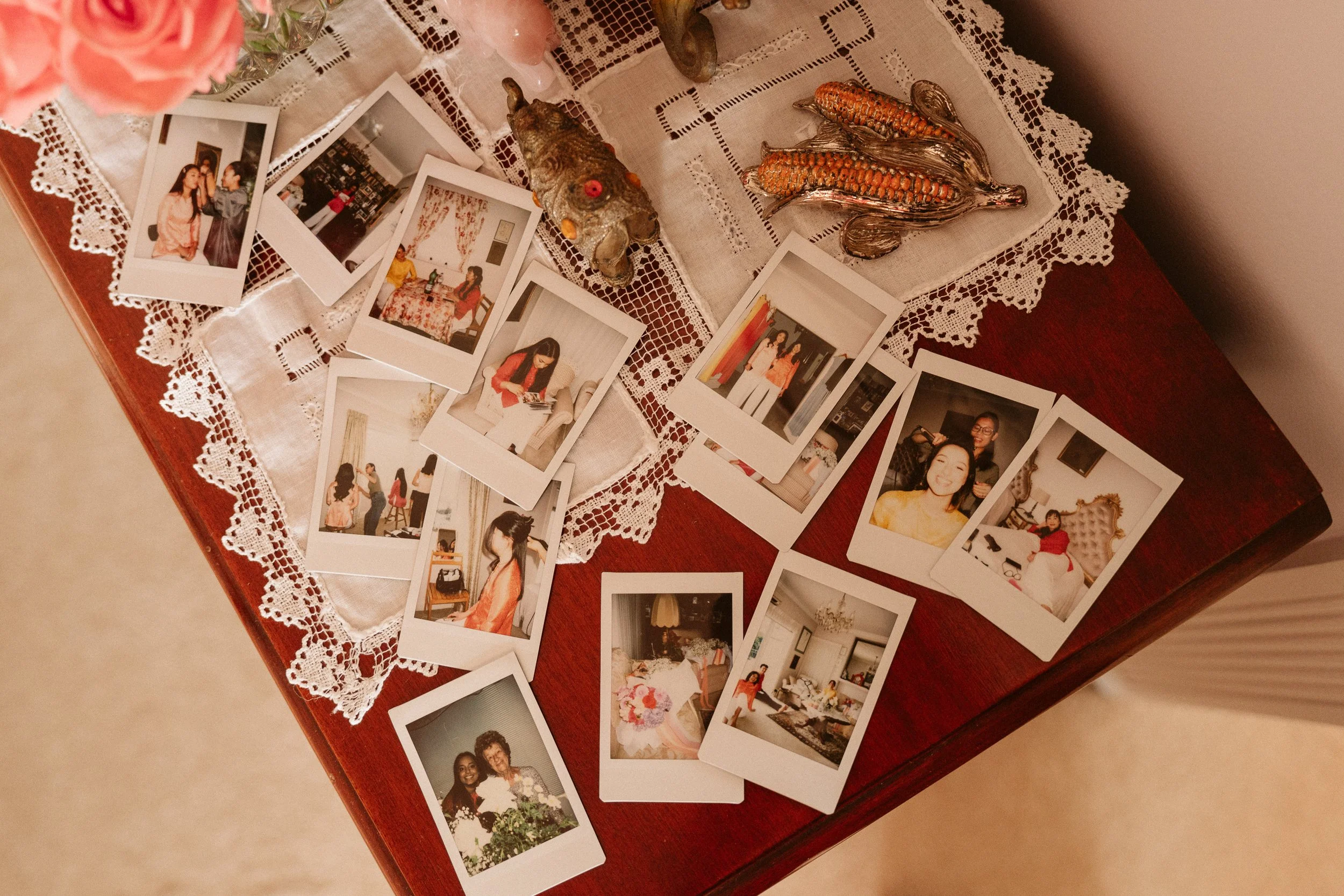 A wooden table decorated with a lace tablecloth holding instant photographs, ceramic animal figurines, and decorative items.
