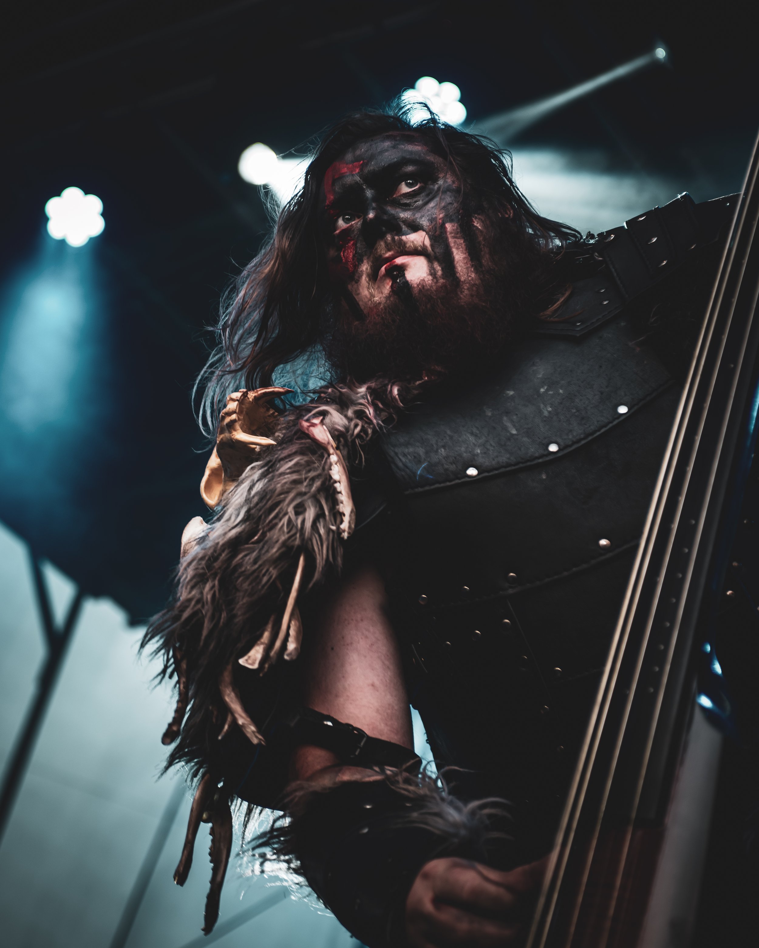 A performer with face paint and medieval-style costume plays an upright instrument on stage under dramatic lighting.