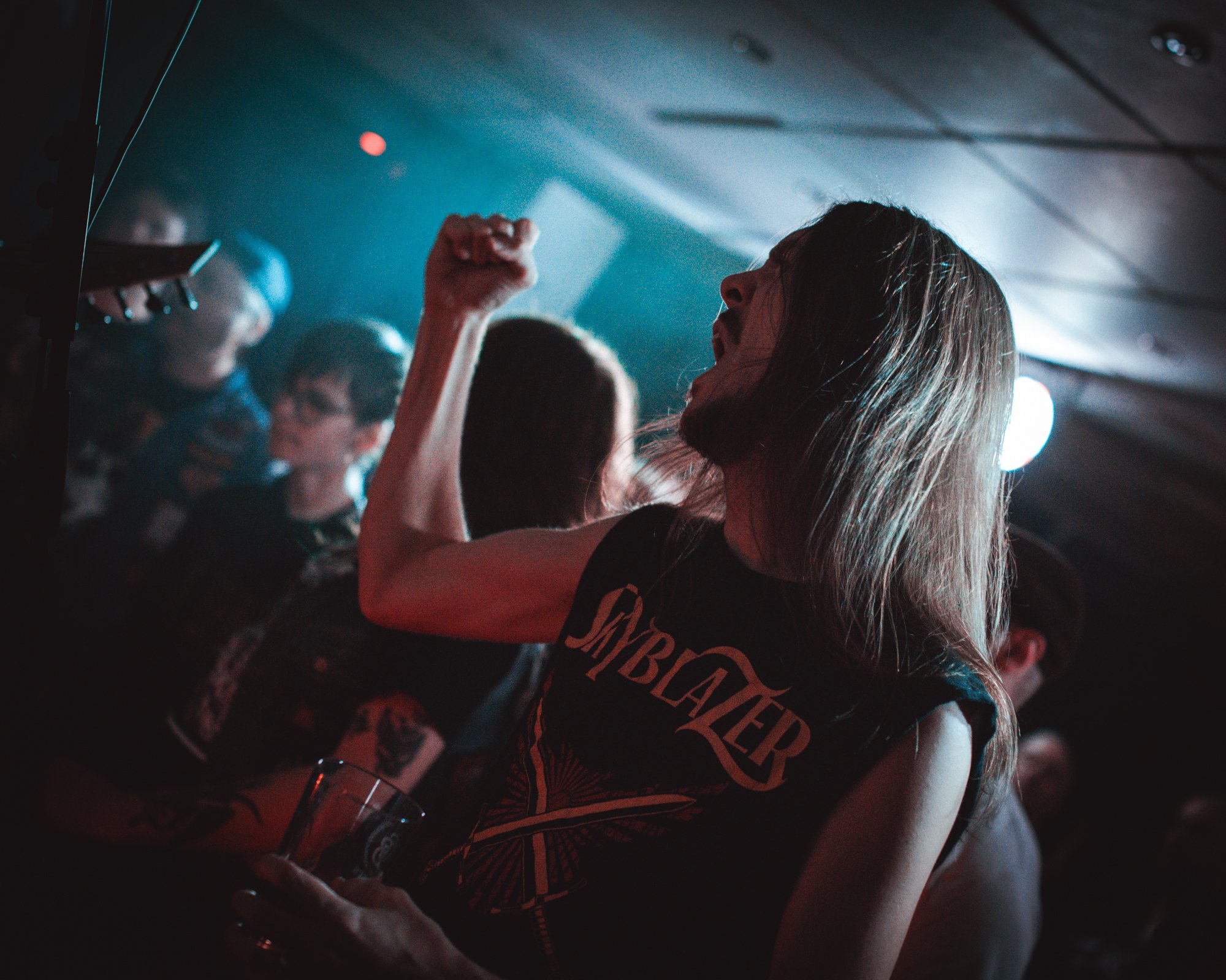 Person with long hair cheering in a dimly lit music venue.