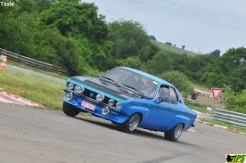 Voiture vintage bleue sur une piste de course avec des arbres en arrière-plan.
