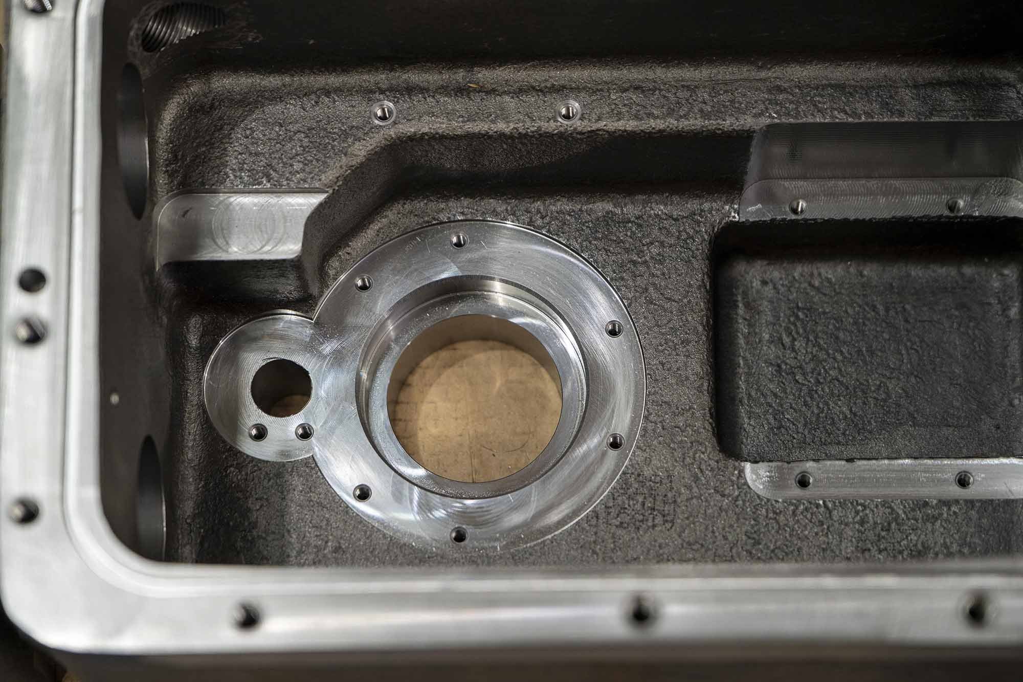 Close-up of a metallic mechanical component with a circular opening and threaded holes, set in a black textured housing.