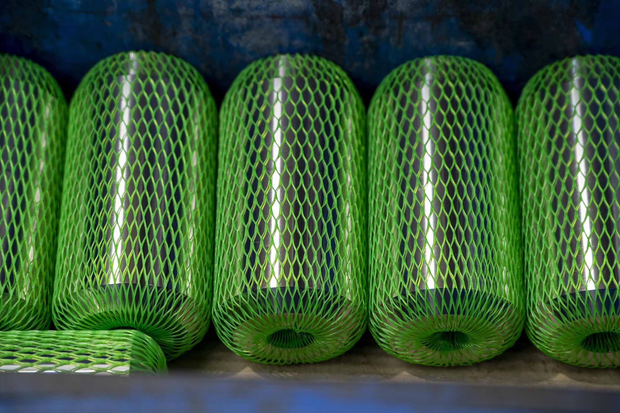 Close-up of green plastic mesh cylindrical objects lined up side by side on a dark surface.
