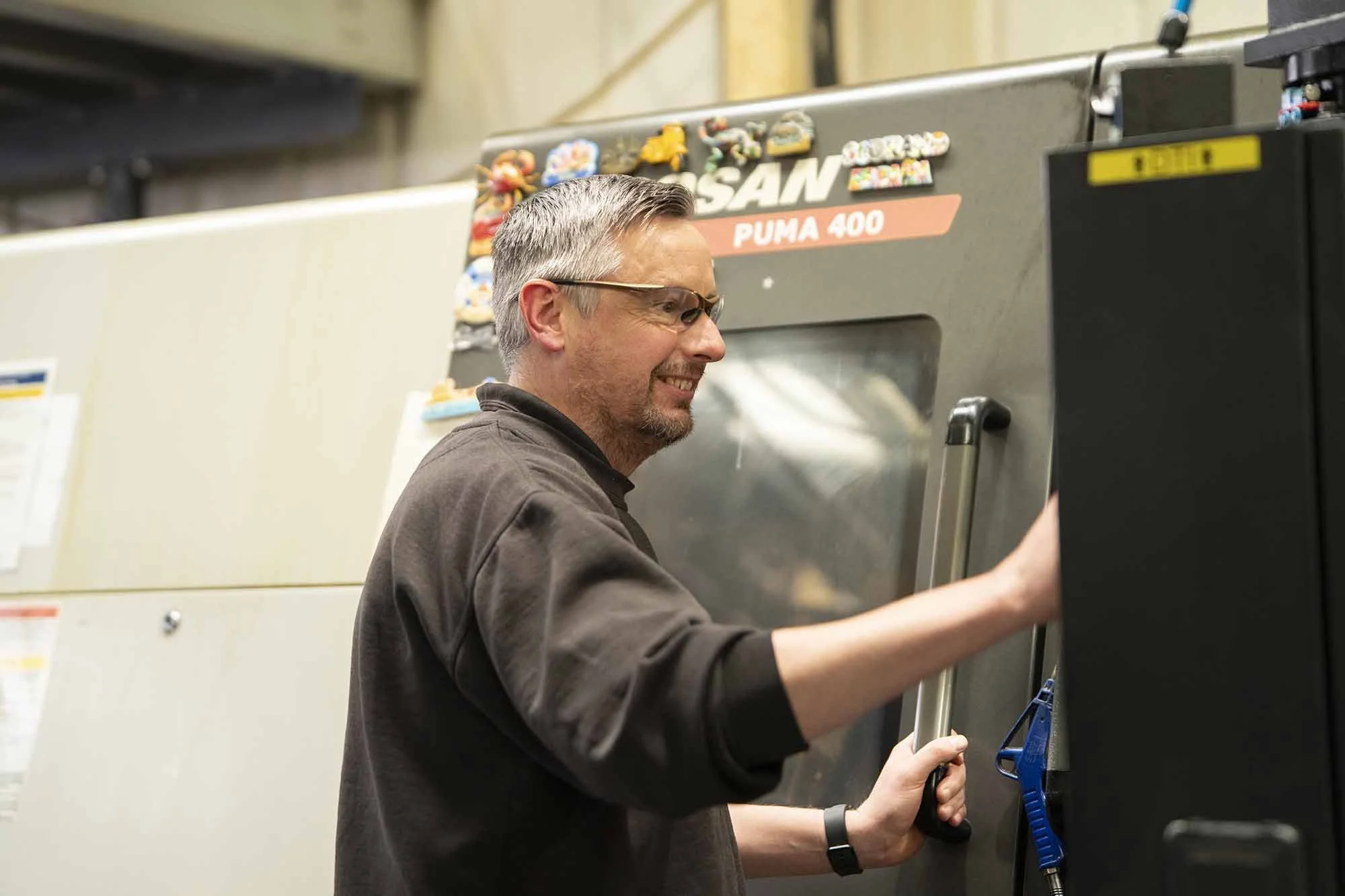 A man with gray hair and glasses working with a large industrial machine labeled 'SAM PUMA 400'.