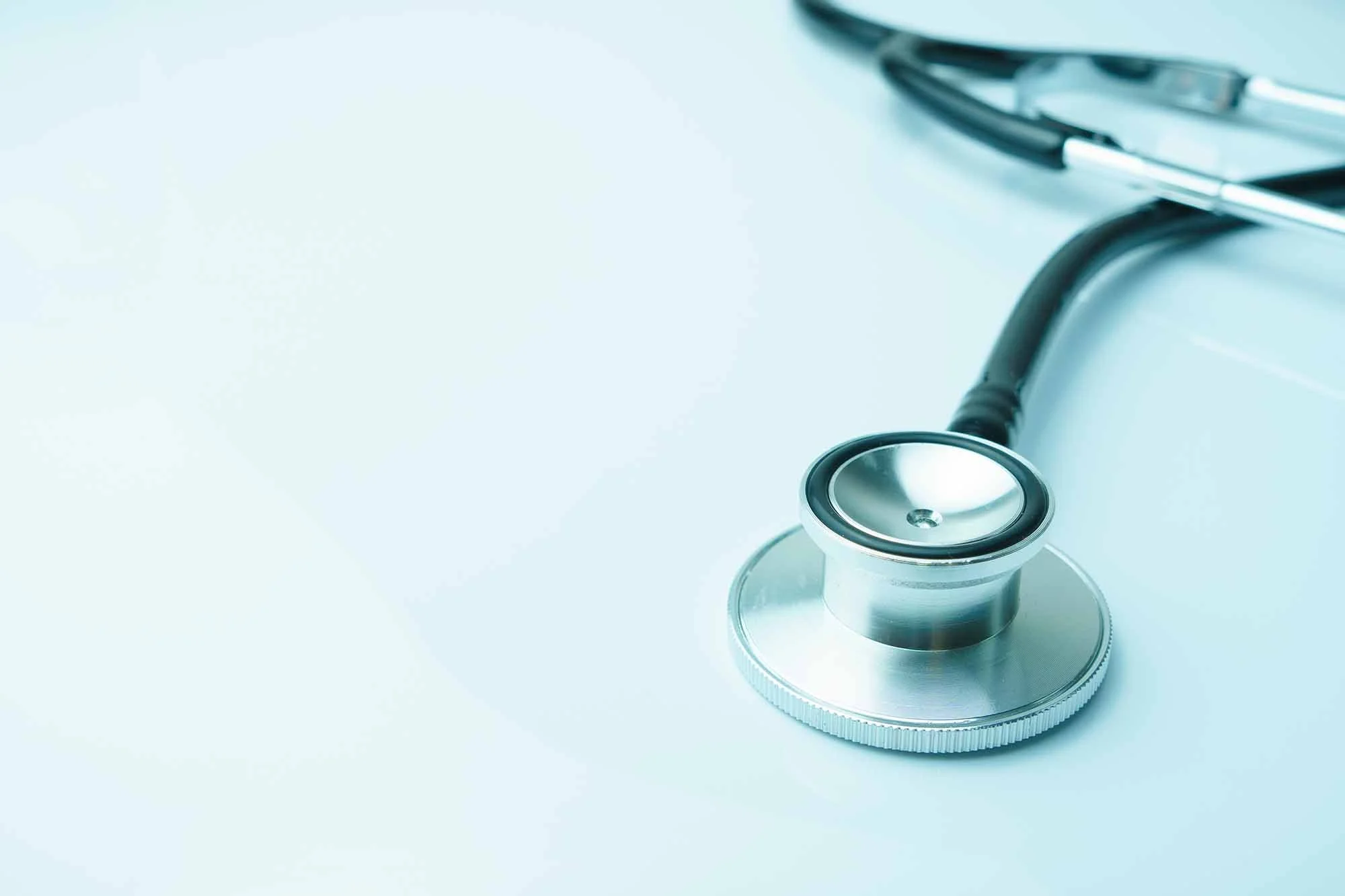 Close-up of a stethoscope on a white medical table, with a pair of glasses partially visible in the background.