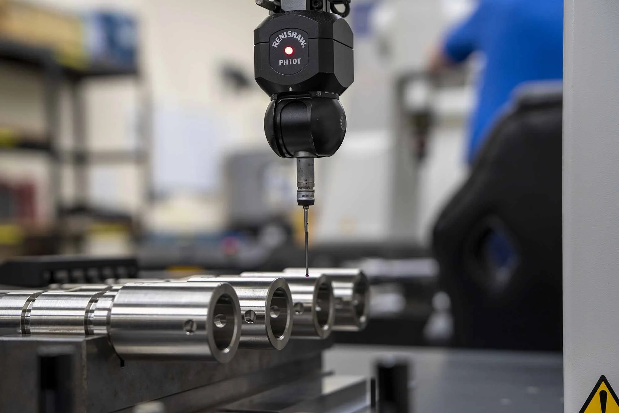 Close-up of a coordinate measuring machine with a digital probe measuring a row of cylindrical metal parts in a manufacturing or laboratory setting.