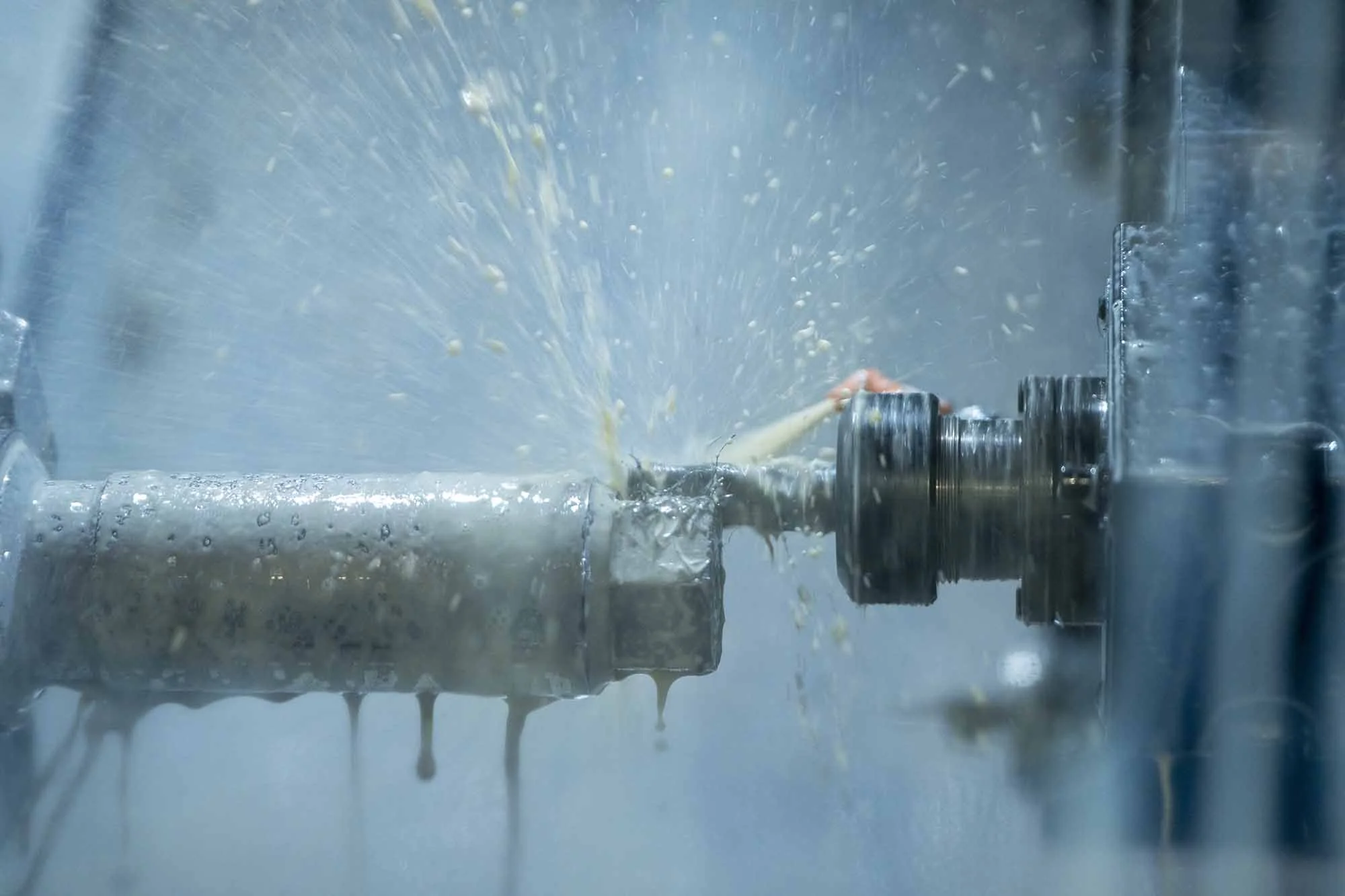 Close-up of a metal machine part being lubricated or cooled with water or oil, with droplets splashing around.
