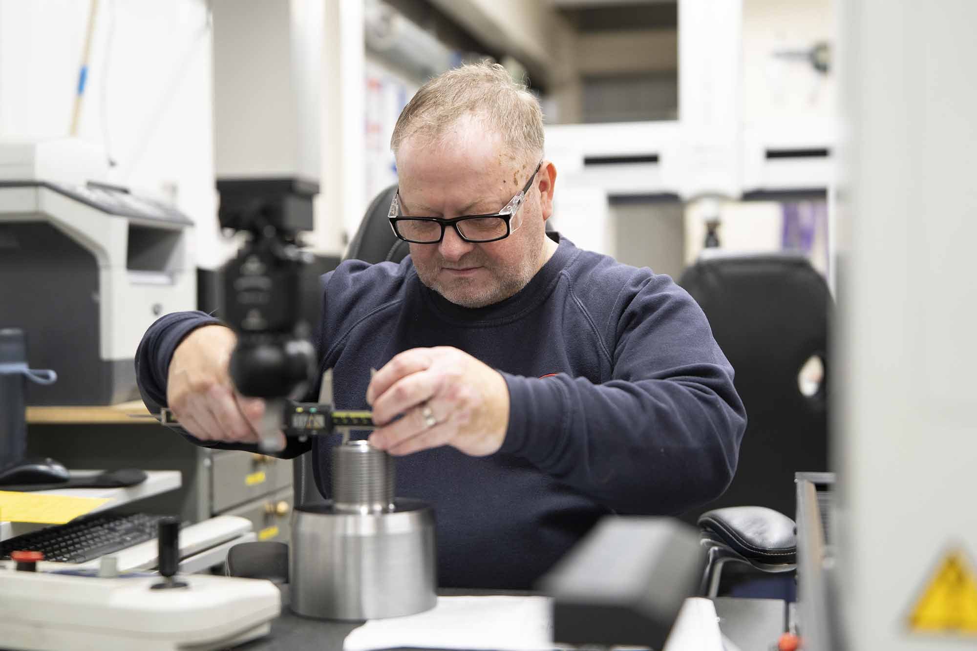 A man with glasses working with equipment at a laboratory table, focused on his task.