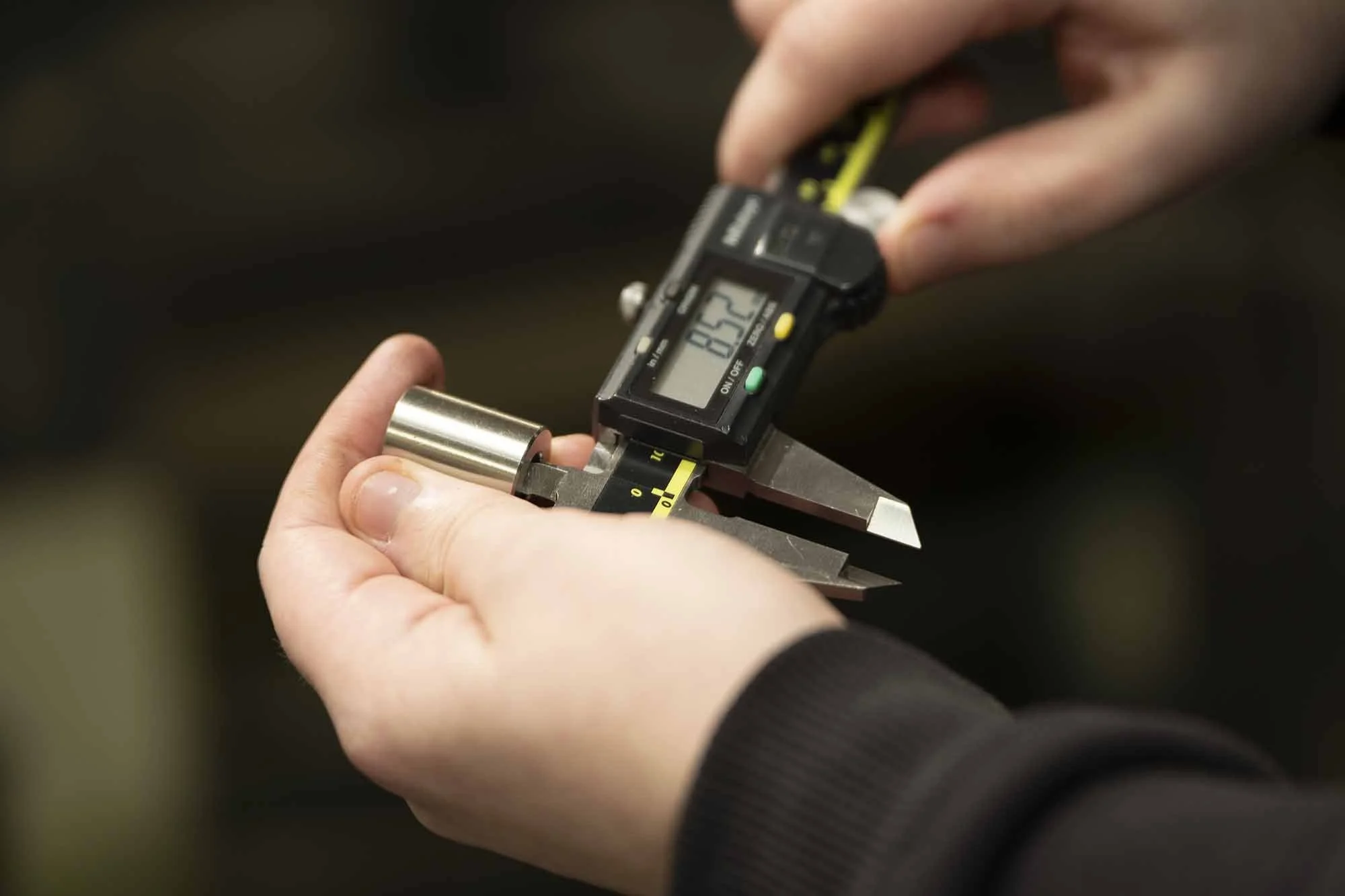 Person measures a metal cylinder's diameter using a digital caliper.