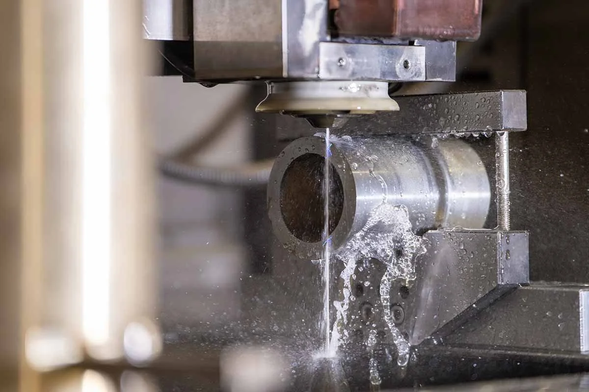 A metal pipe is being cut on a CNC machine, with water coolant spraying onto the cut area.
