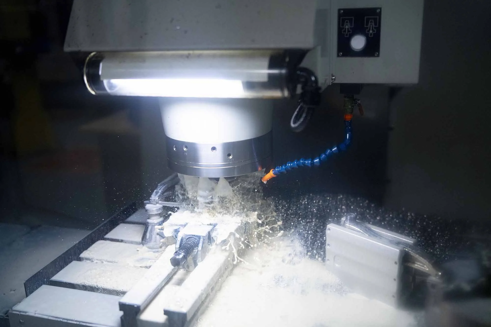A CNC machine cutting a piece of metal, with coolant or lubricant being sprayed on the cutting area.