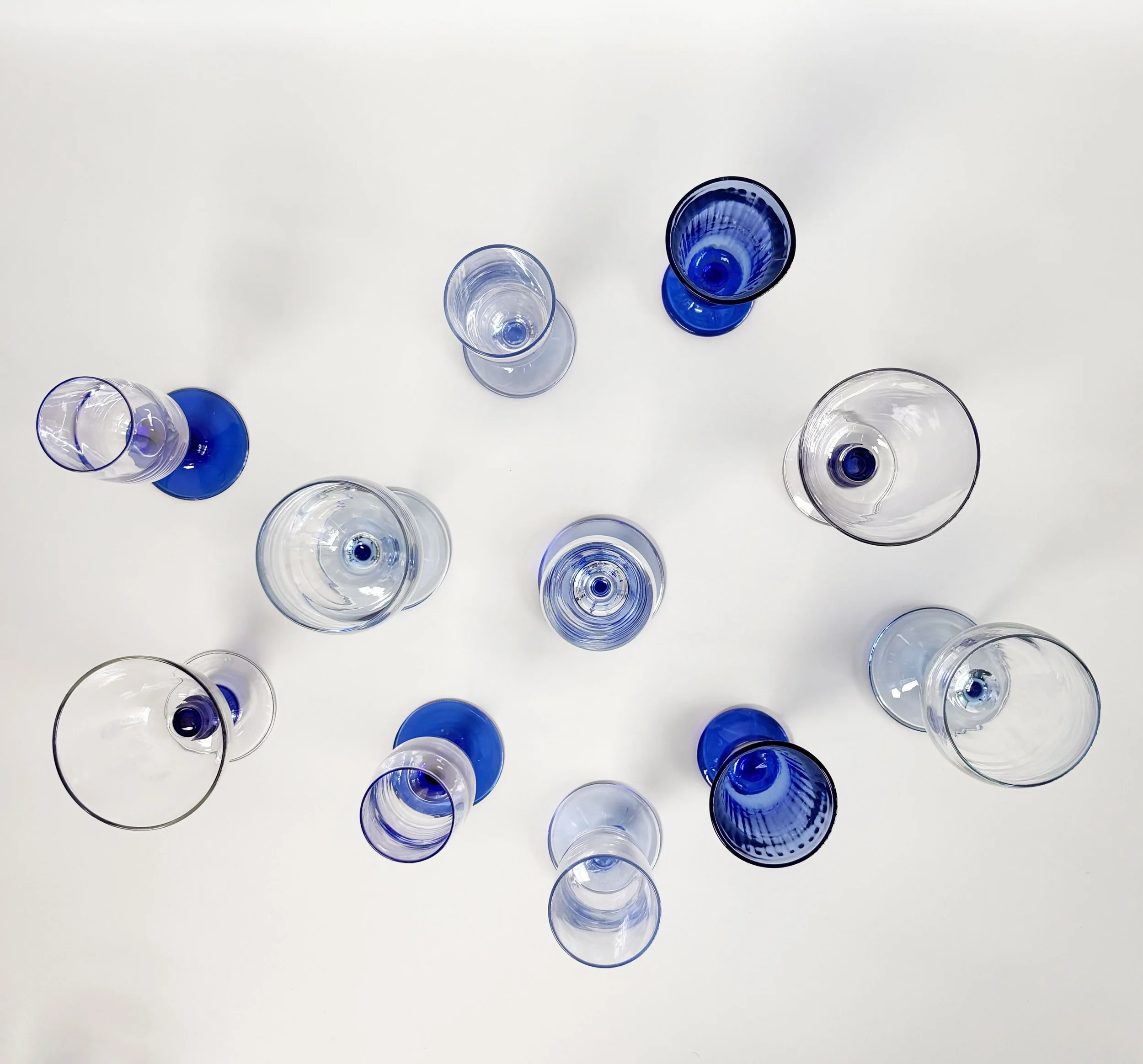 Top-down view of multiple empty glass cups and vases in clear and blue colors arranged on a white surface.