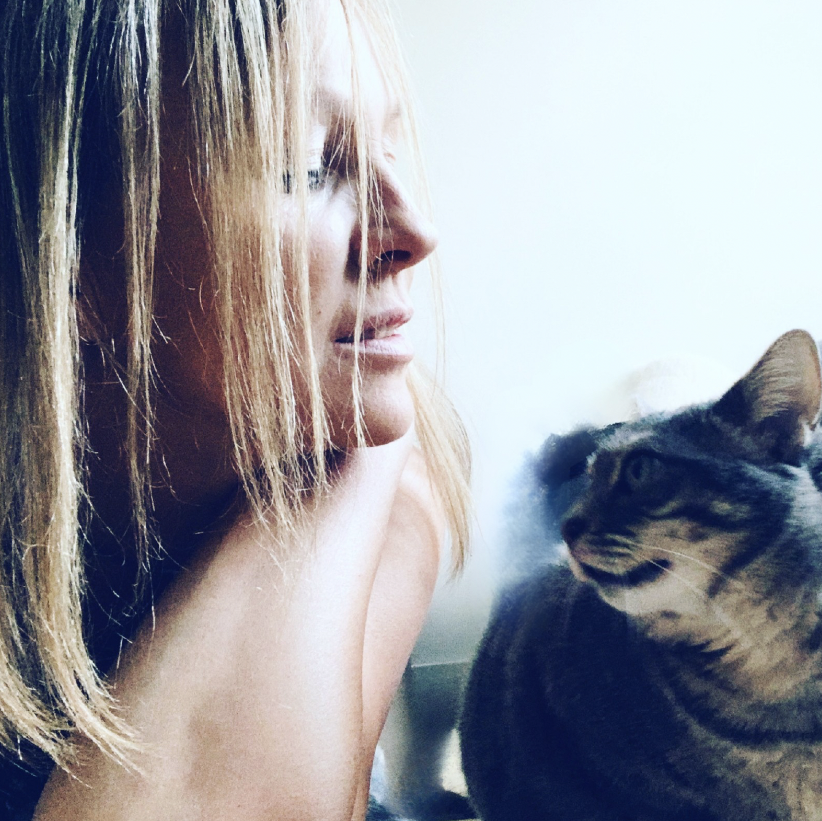 Une femme aux cheveux roux regarde un chat tigré qui la regarde.
