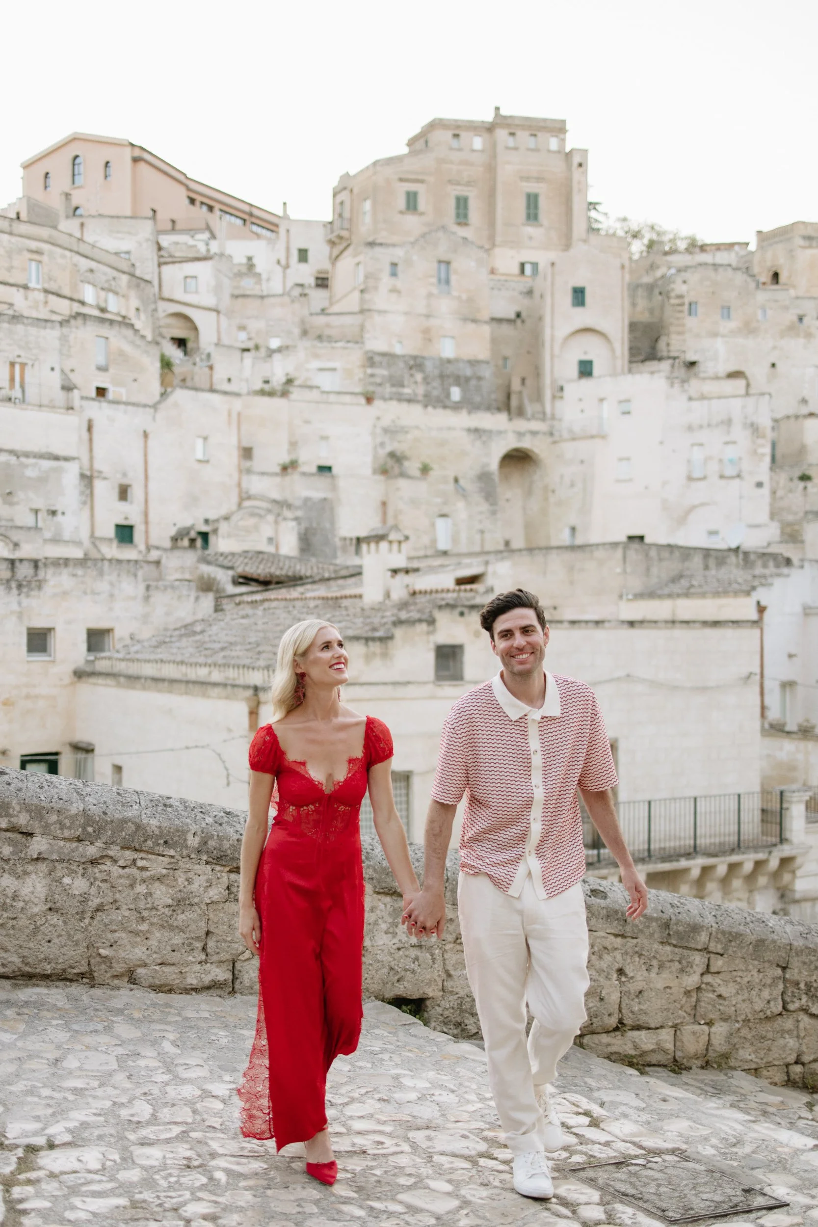 Bride and groom walking through the streets of Matera Italy at destination wedding in red lace dress with pointed slingback heels