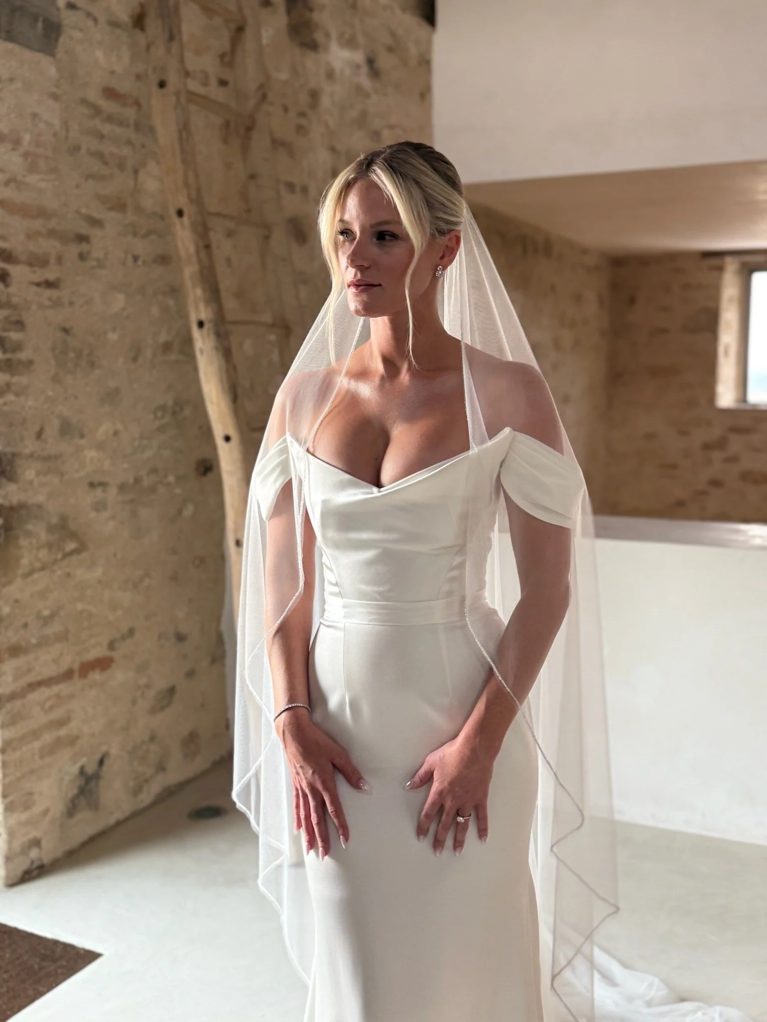 A bride wearing a white wedding gown and veil, standing inside a rustic stone-walled room with wooden accents in Italy.