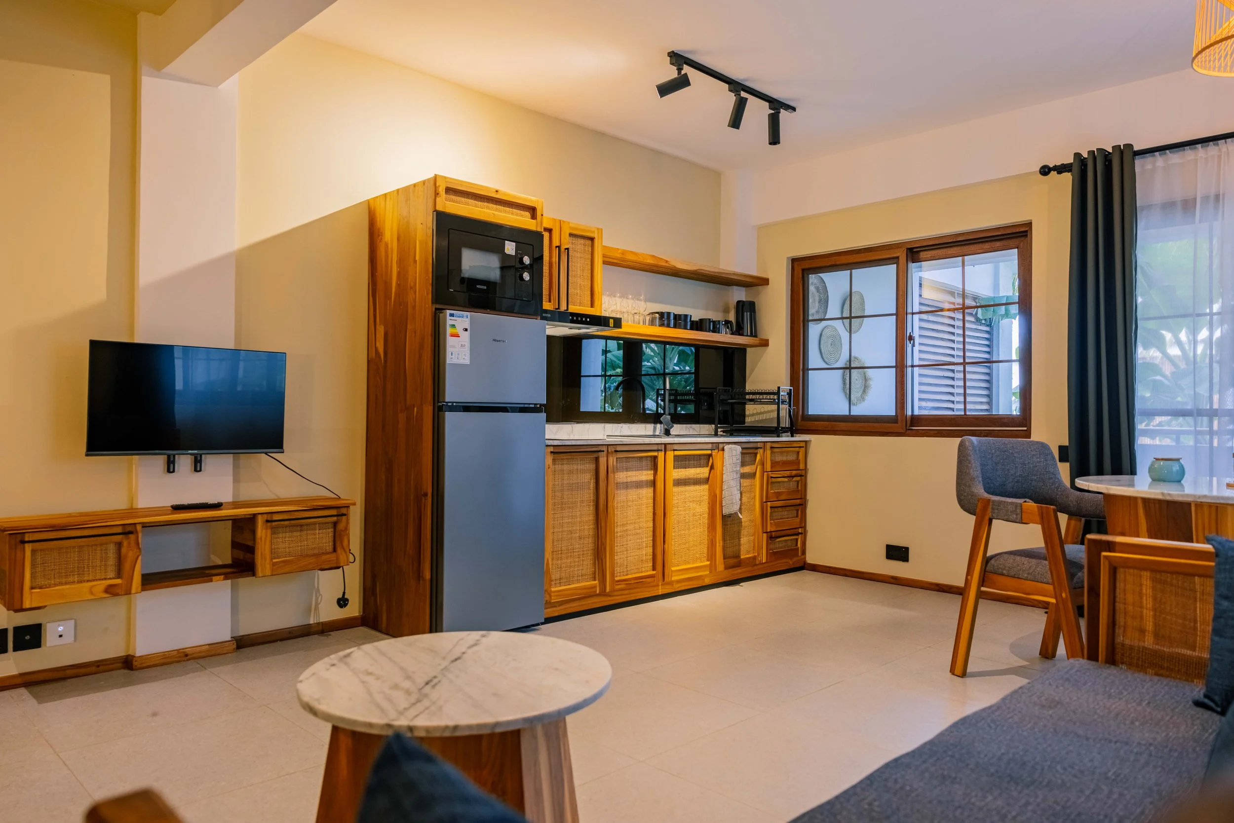 Living room with wooden cabinetry, a mounted flat-screen television, large windows with curtains, and a dining table with chairs.