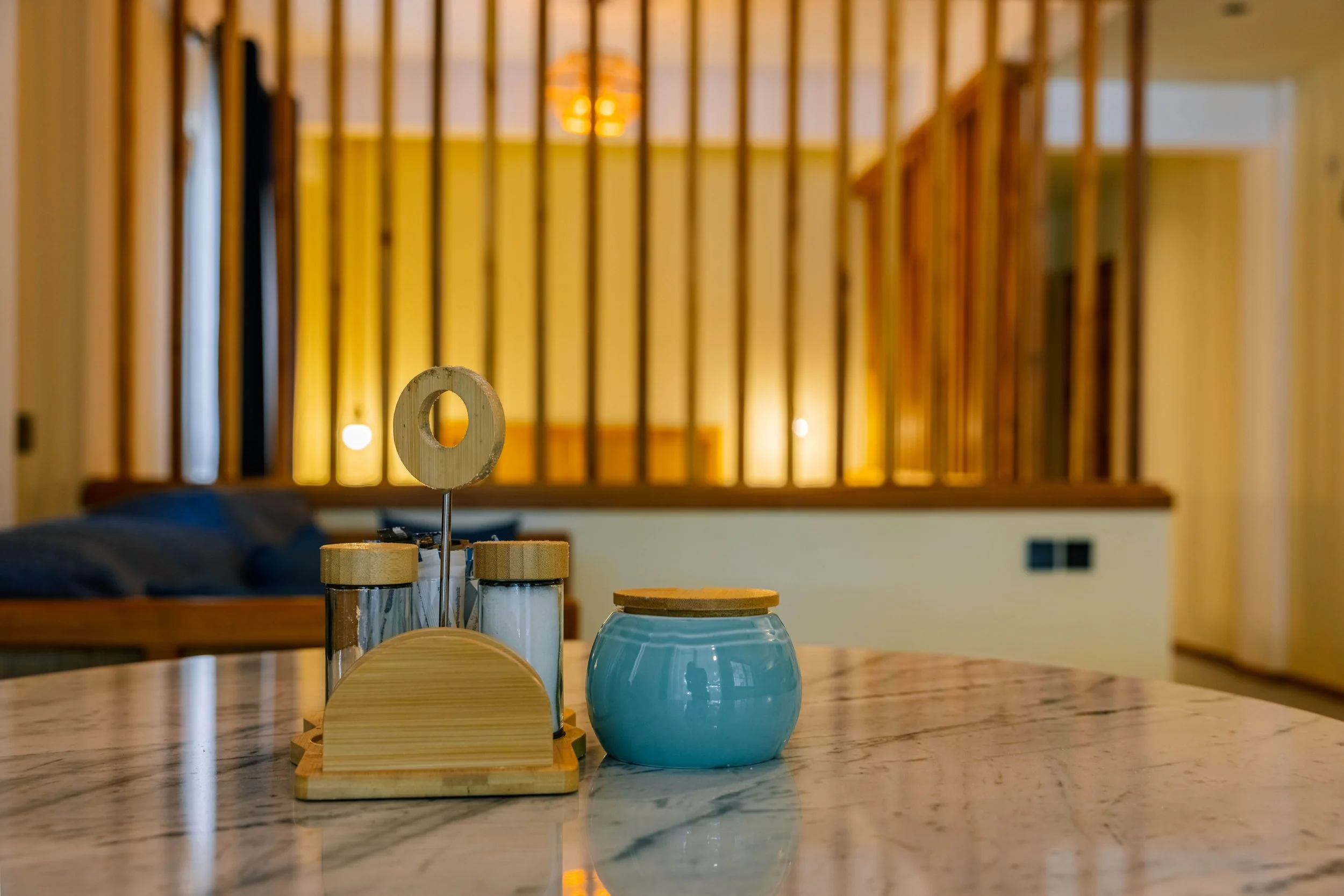 A wooden table with condiment containers, including a salt and pepper shaker and a small glass, in a room with wooden paneling and a staircase in the background.