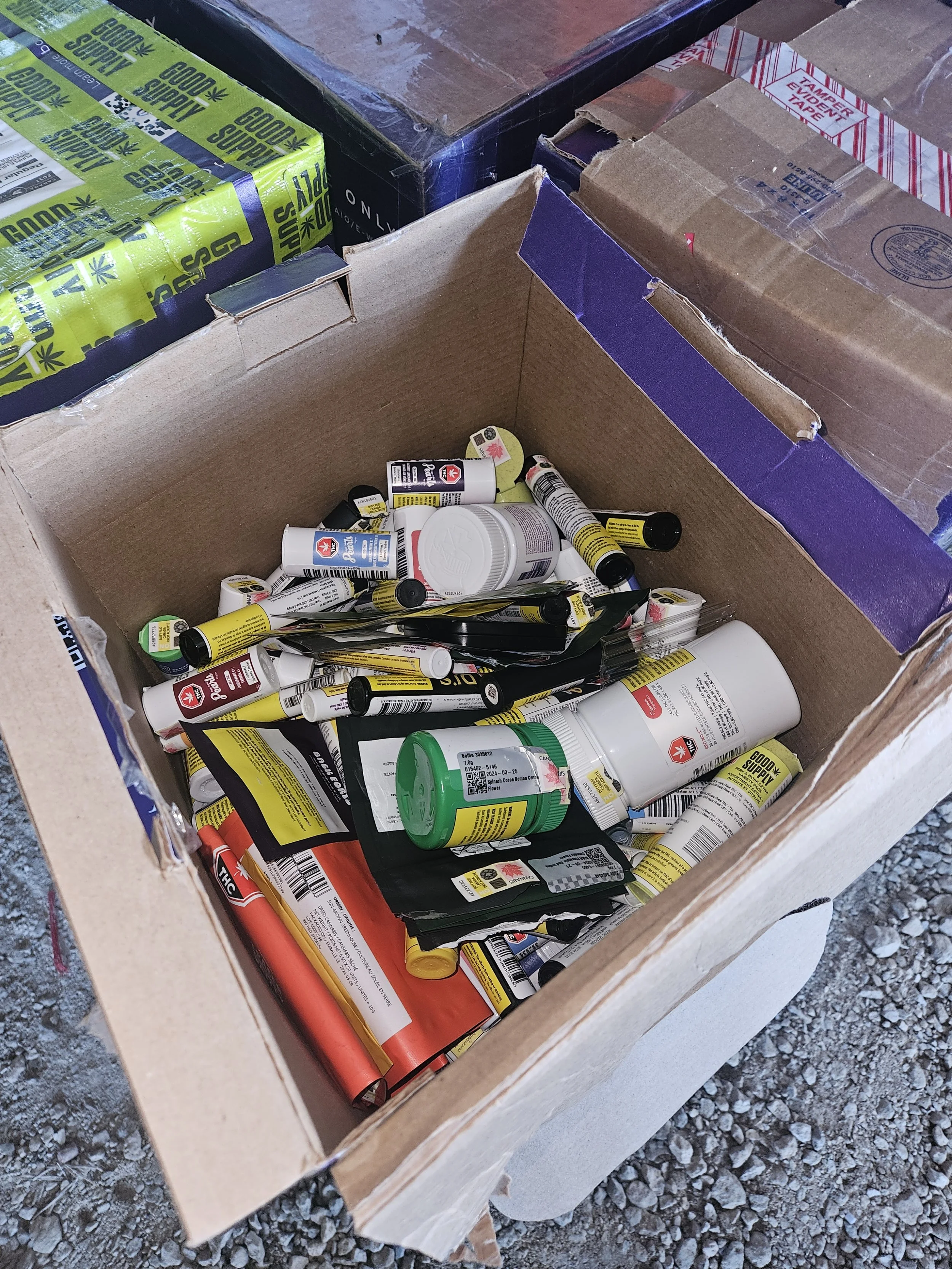 Open cardboard box containing various drug and supplement bottles and packets.