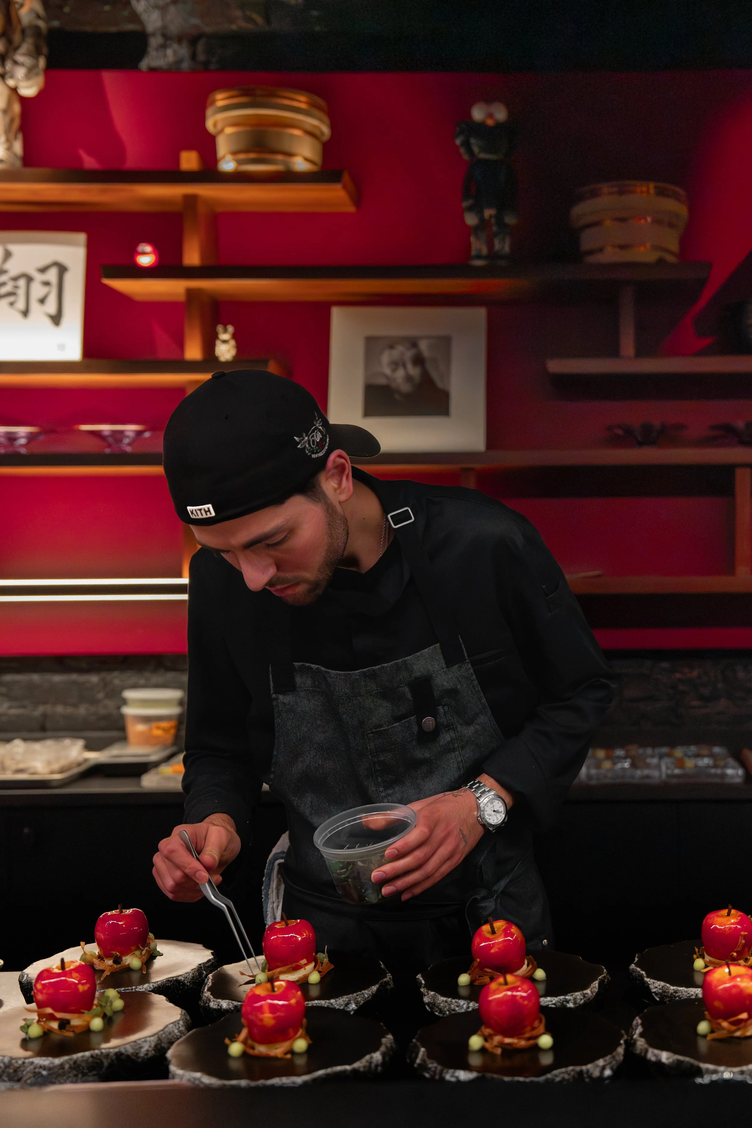 Chef preparing multiple decorated desserts with red apples on black plates.
