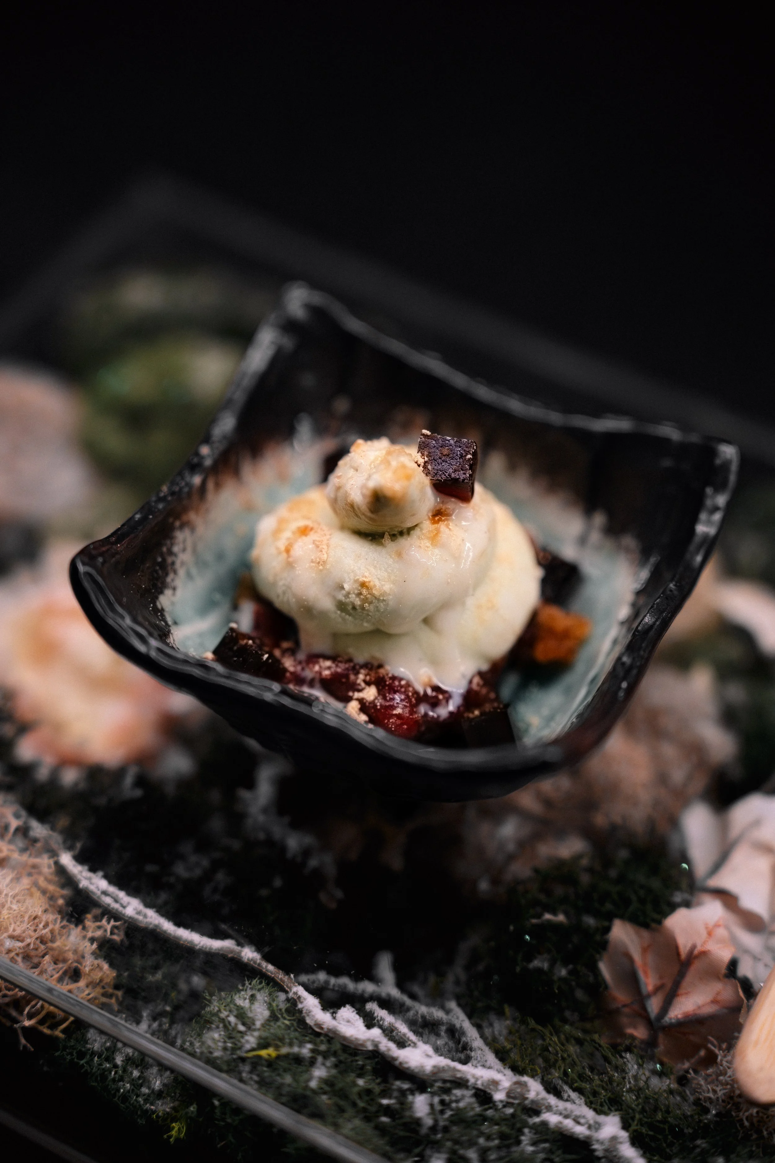 A scoop of vanilla ice cream topped with chocolate pieces in a small black dish.