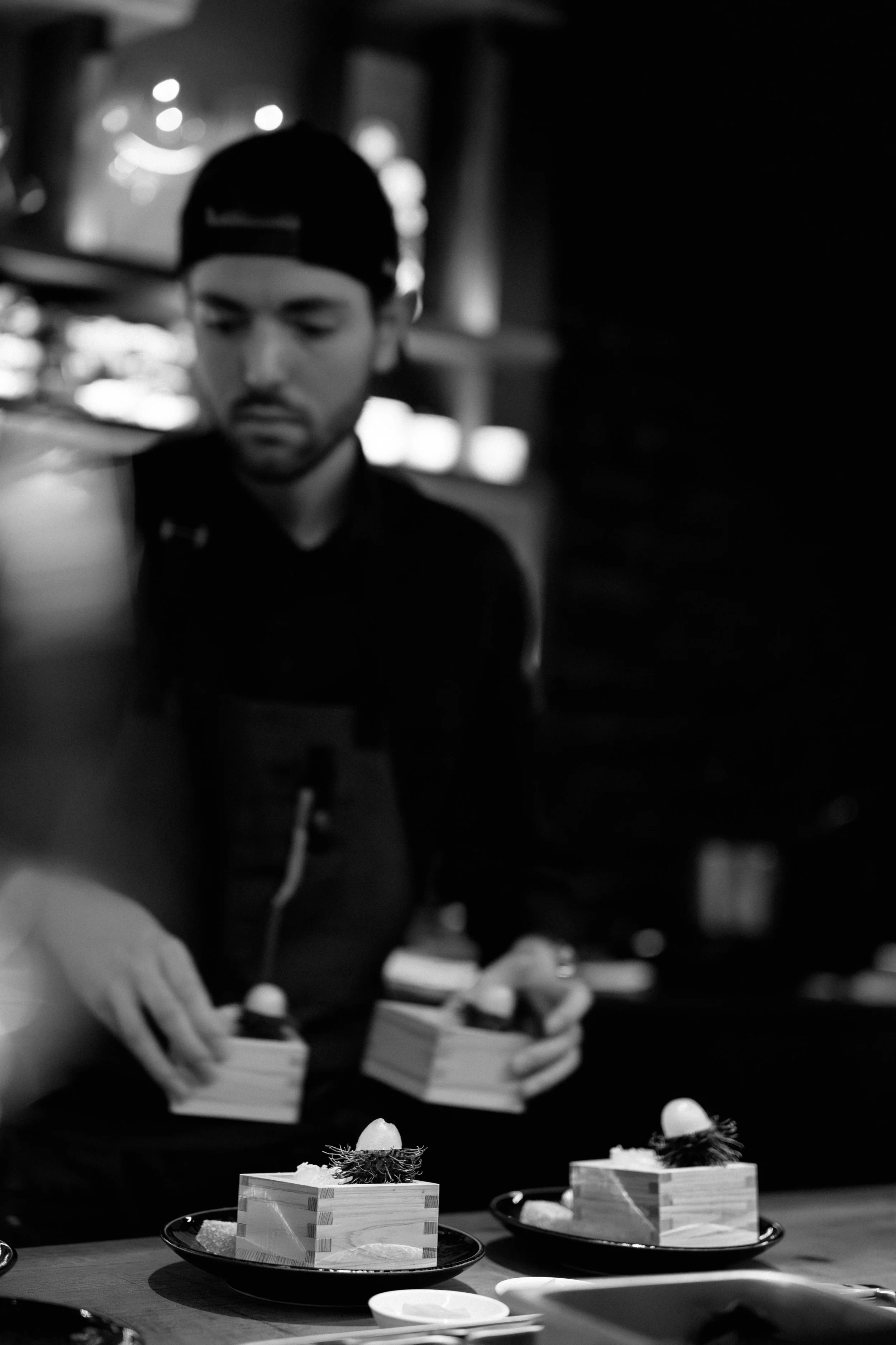 A chef preparing dishes with small wooden boxes topped with eggs and garnishes on a serving tray.