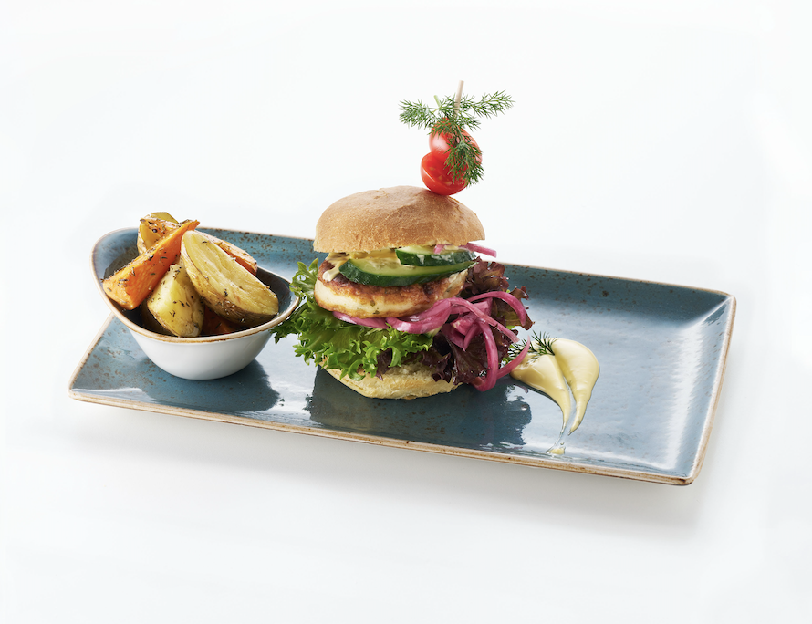 A gourmet burger with lettuce, cucumber, pickles, and pickled onions on a bun, garnished with a cherry tomato and dill, served with roasted potato wedges and a dollop of mayonnaise on a blue rectangular plate.
